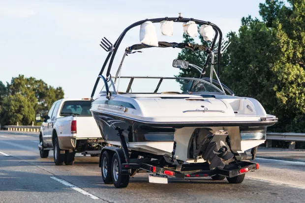 Boat being towed on a trailer behind a white SUV on a road.