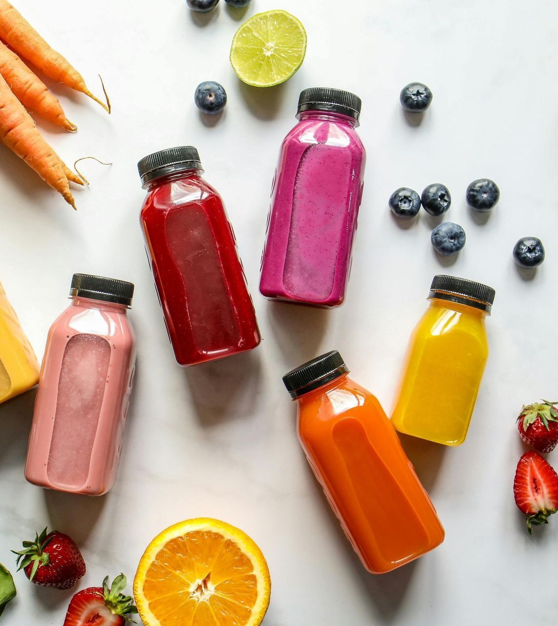 Bottles of colorful juice with surrounding fruits and vegetables.