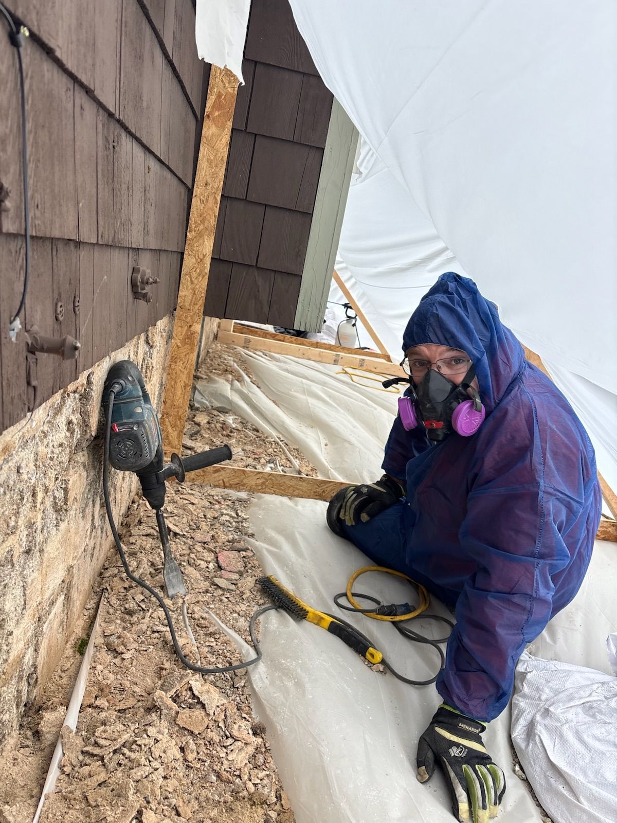 Person in protective suit using a drill, working on a building's exterior.