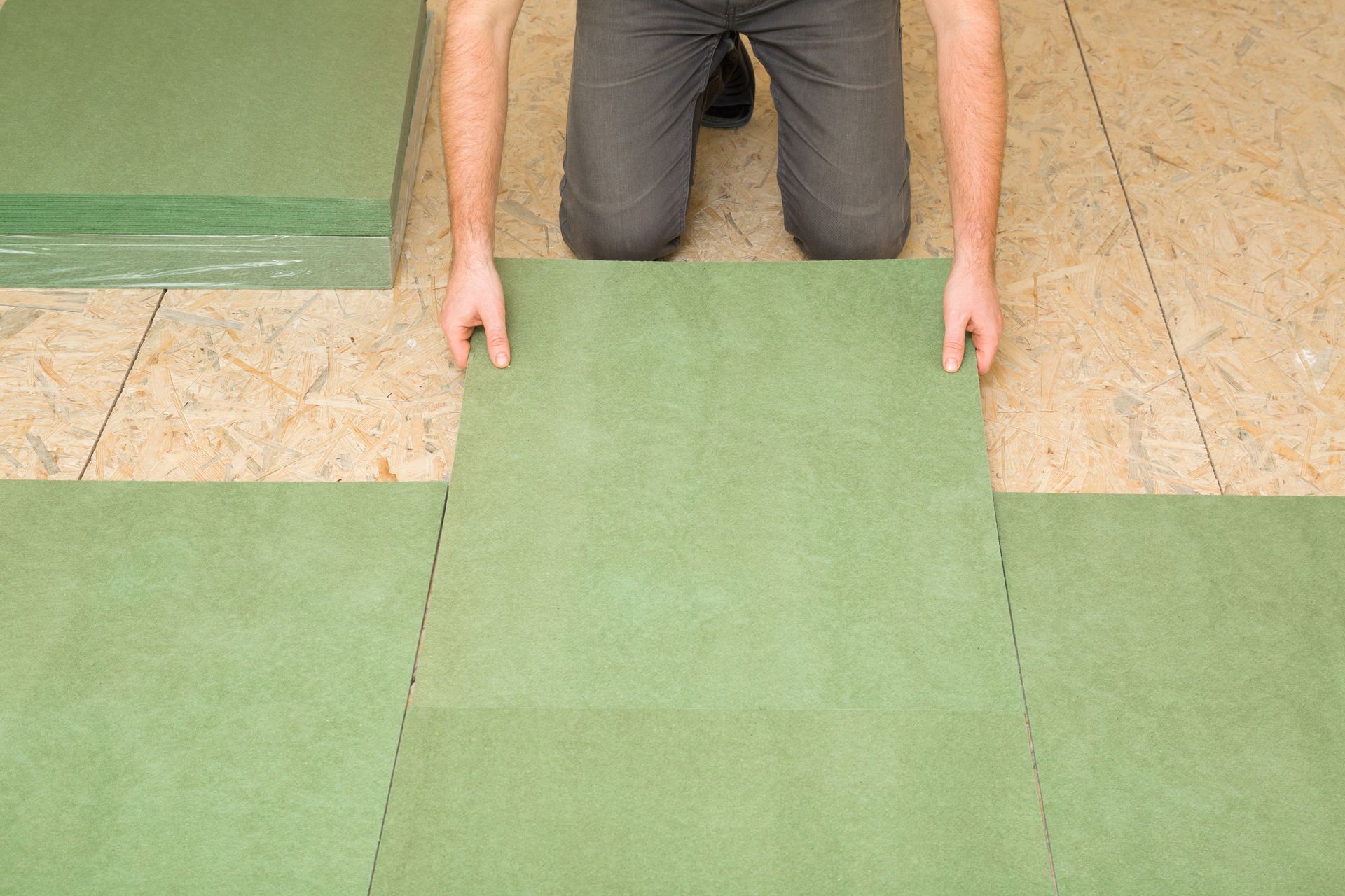 Person installing green soundproofing floor tiles on a wooden subfloor.