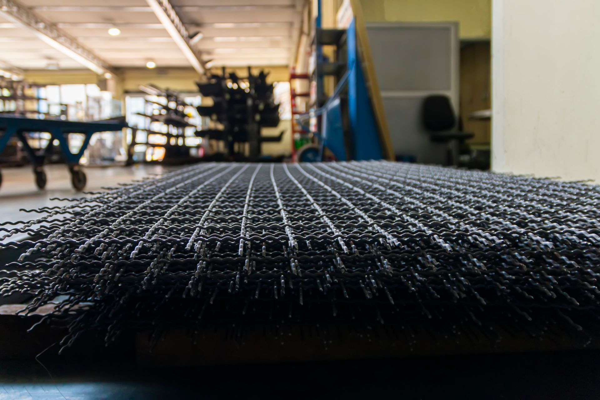 Black woven wire mesh screen close-up in an industrial warehouse.
