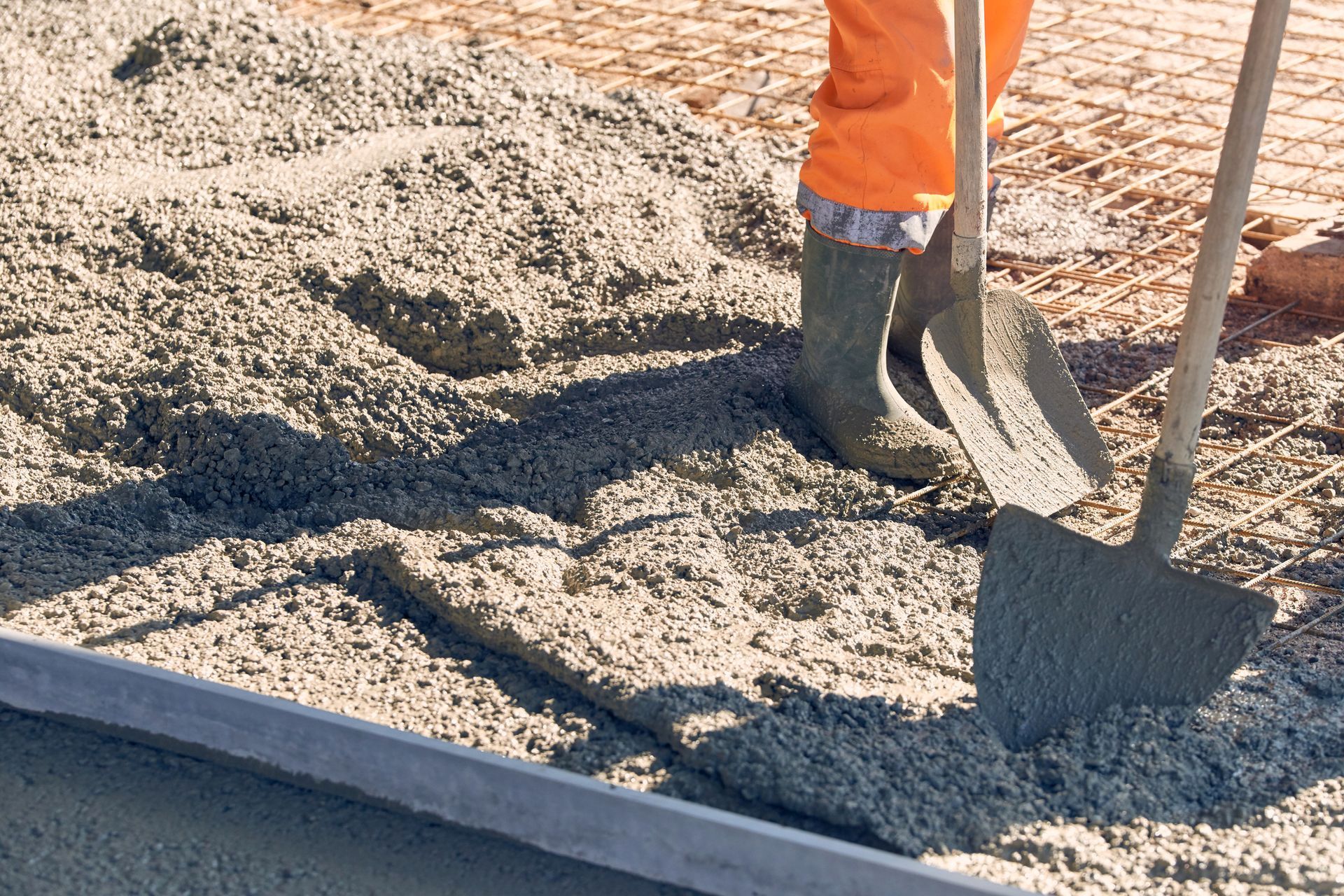 Worker leveling wet concrete on steel rebar for slab foundation construction.