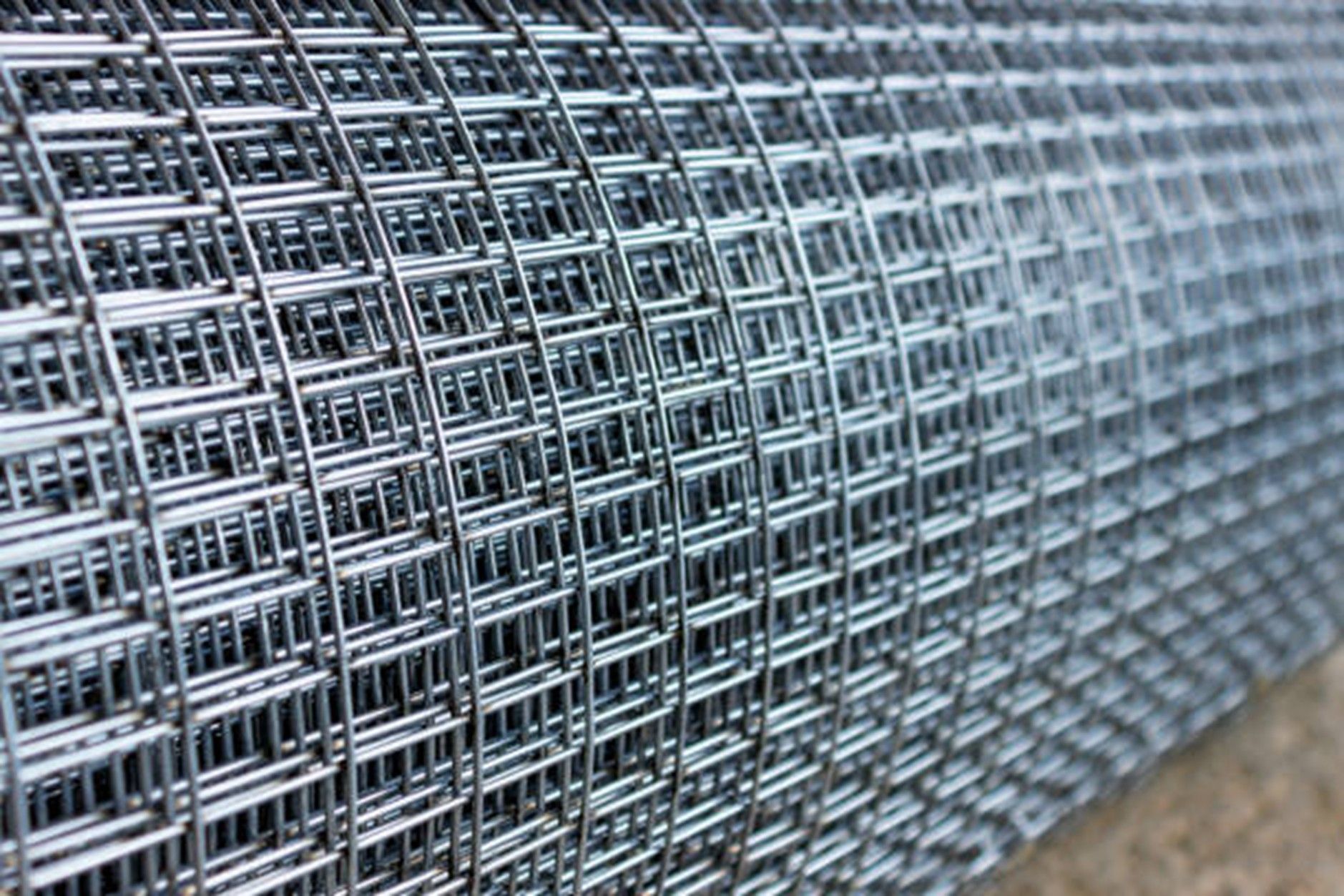 A close-up roll of galvanized welded wire mesh fencing with a grid pattern.