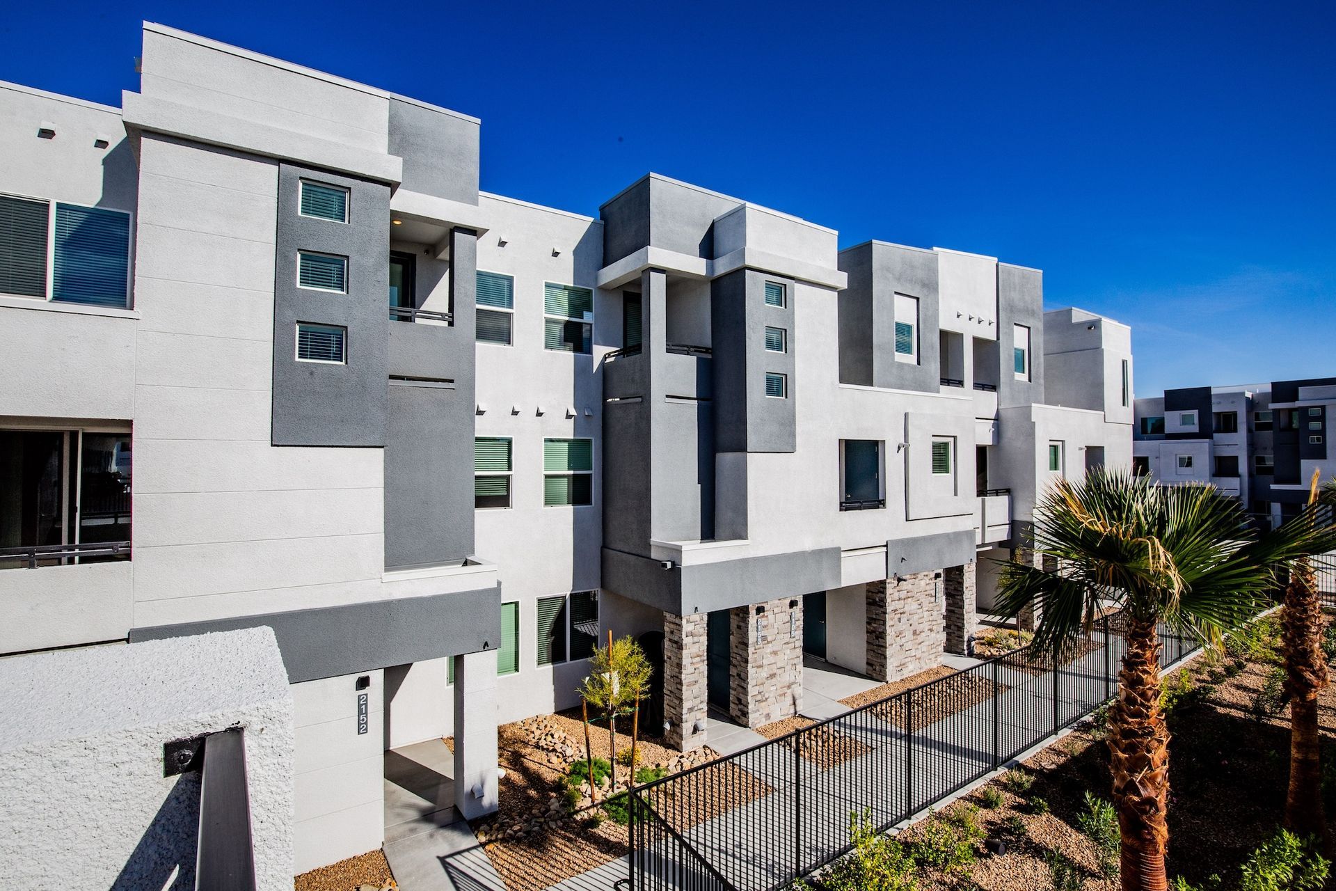 Modern three-story townhomes with white and gray exteriors under a clear blue sky.