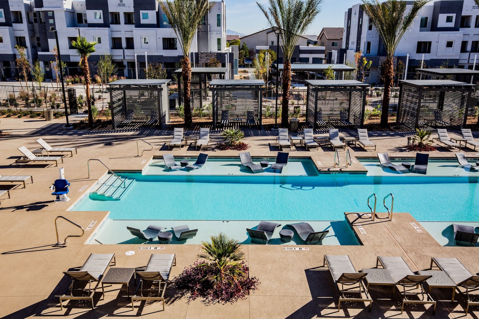 Swimming pool area with lounge chairs, cabanas, and modern buildings.