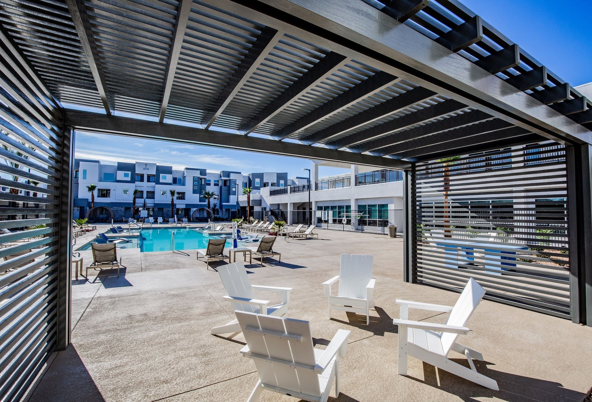 Patio with white chairs overlooking a pool area. Apartment buildings in the background.