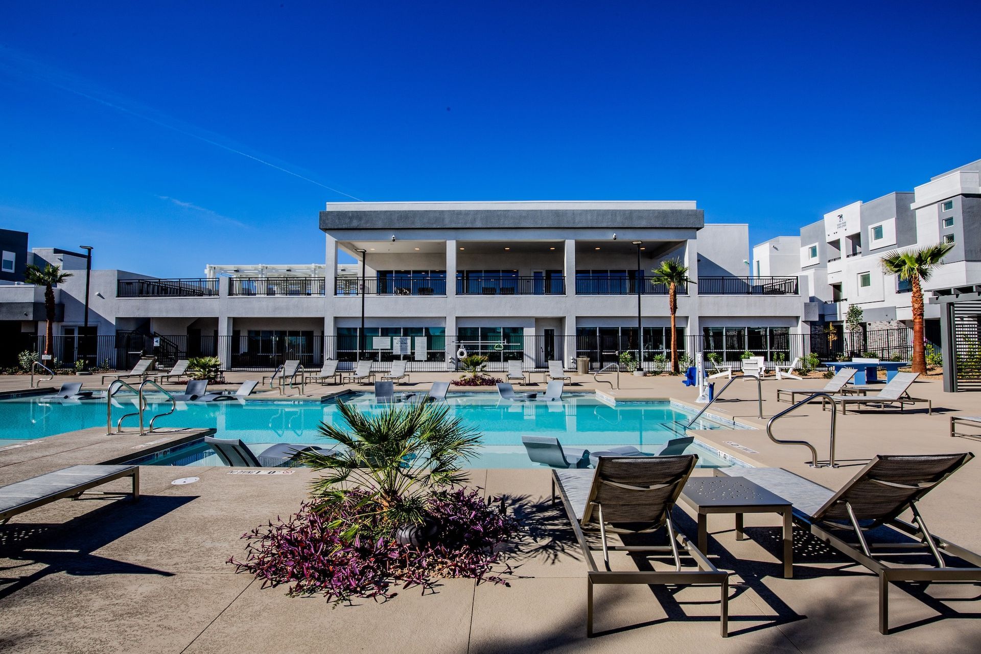 Pool area with lounge chairs, building, and clear blue sky.
