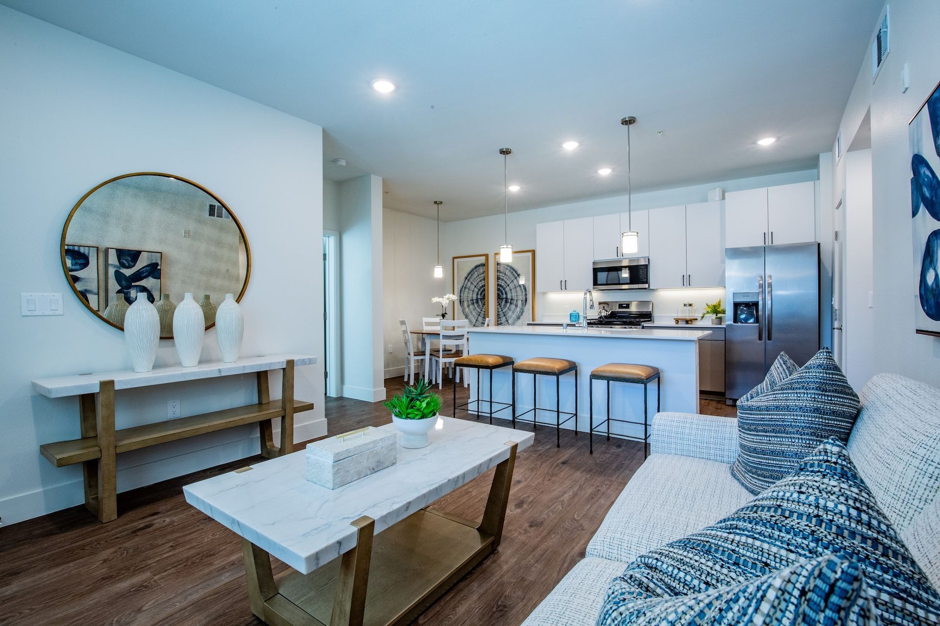 Bright, modern apartment interior with kitchen, living room, and wooden floors. White and blue accents, stainless steel appliances.