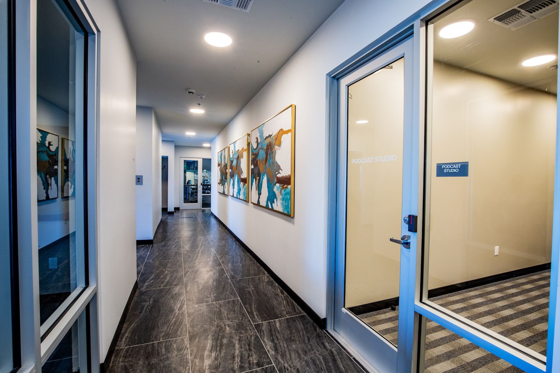 Long hallway with dark flooring, glass doors, artwork, and recessed lighting.