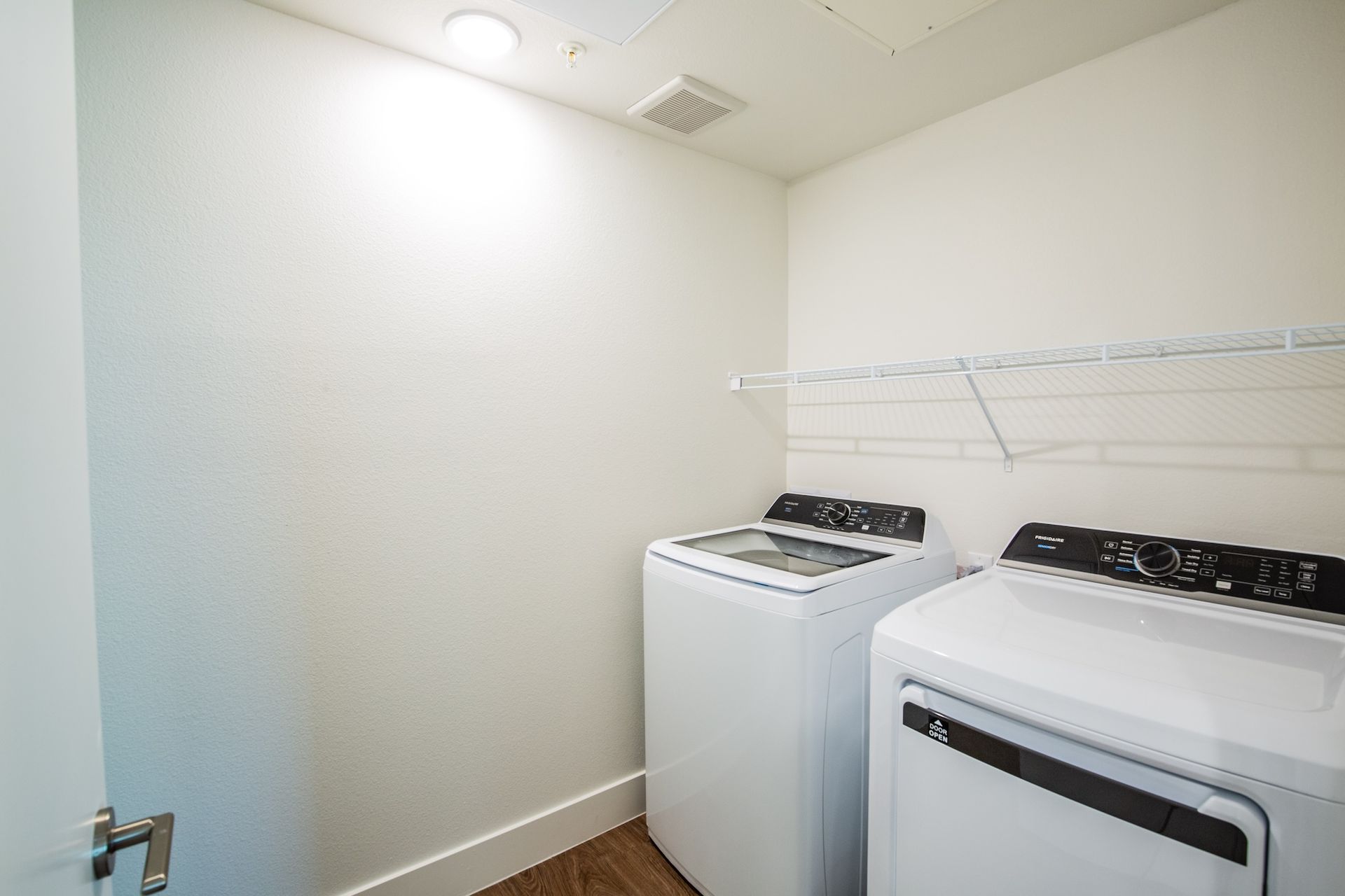 Laundry room with white washer and dryer, shelf, and door.