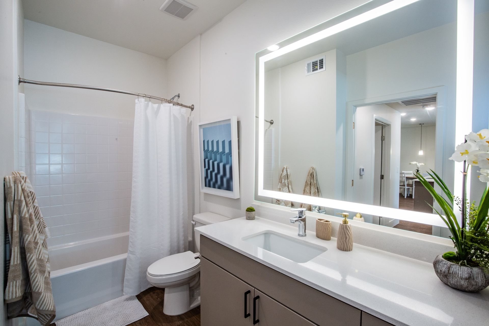 Modern bathroom with white walls, gray vanity, backlit mirror, and a shower with a white curtain.