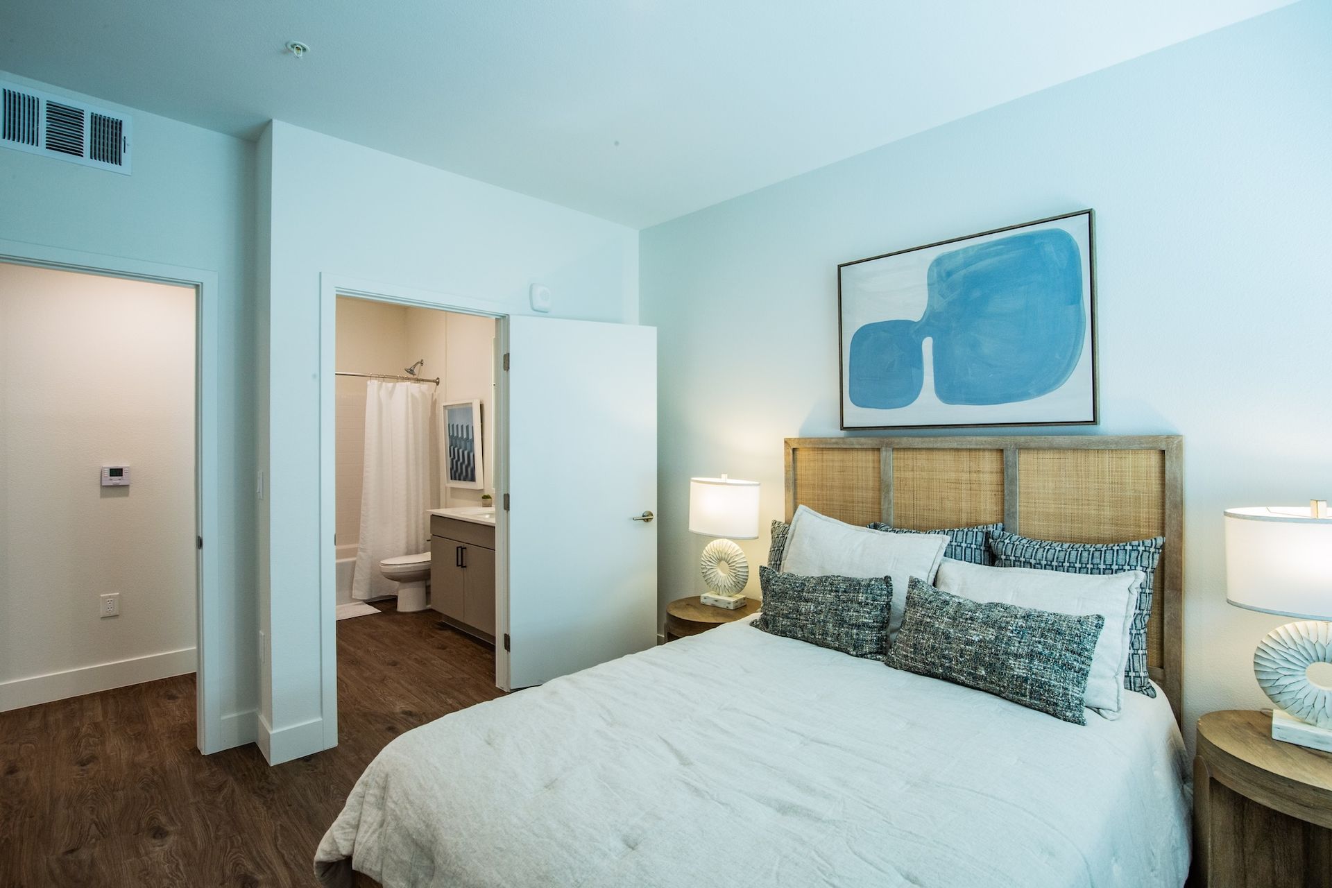 Bedroom with bed, art, and open bathroom door, neutral colors.