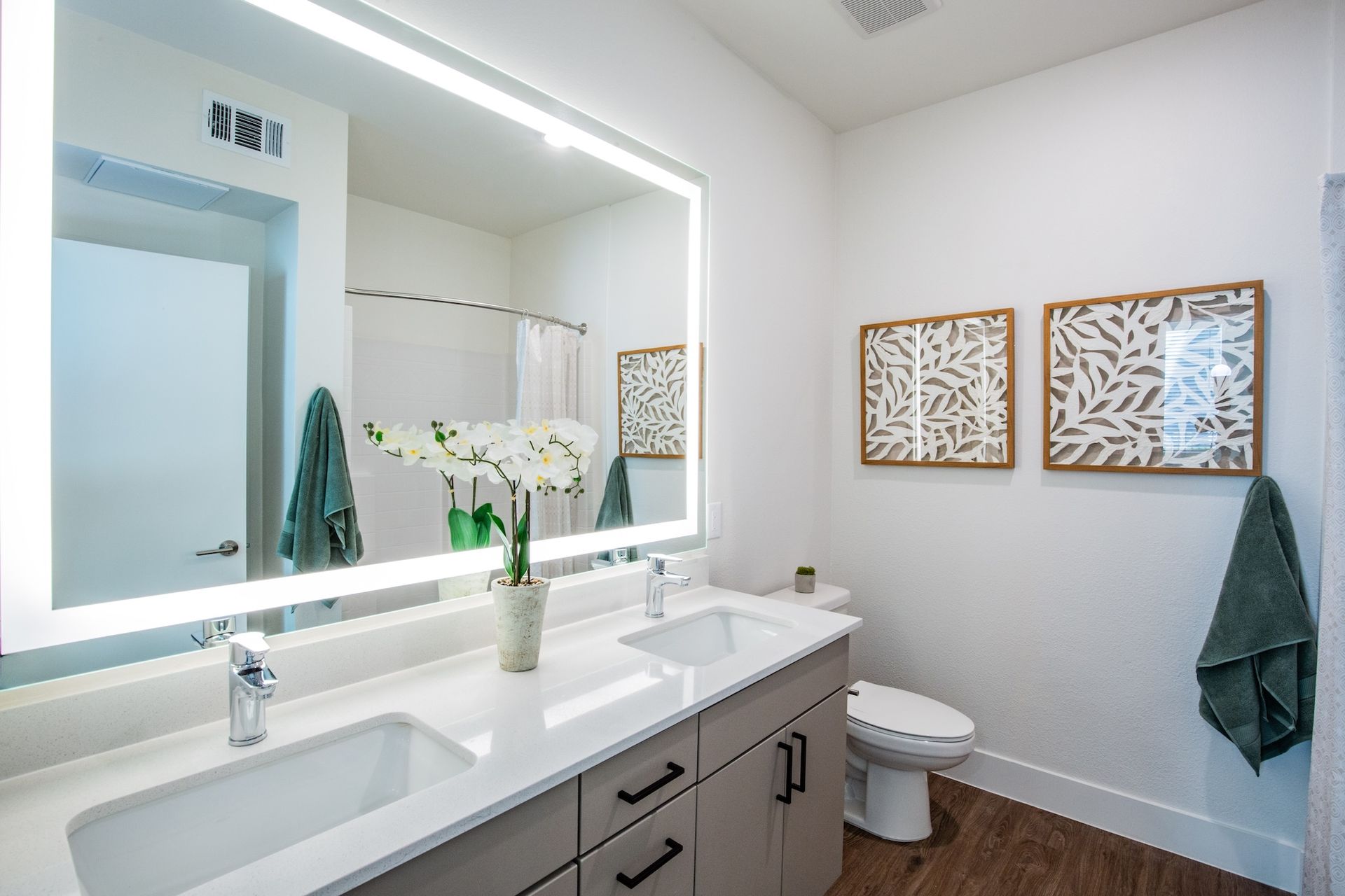 Modern bathroom with double sink vanity, large mirror with lights, and decorative wall art.