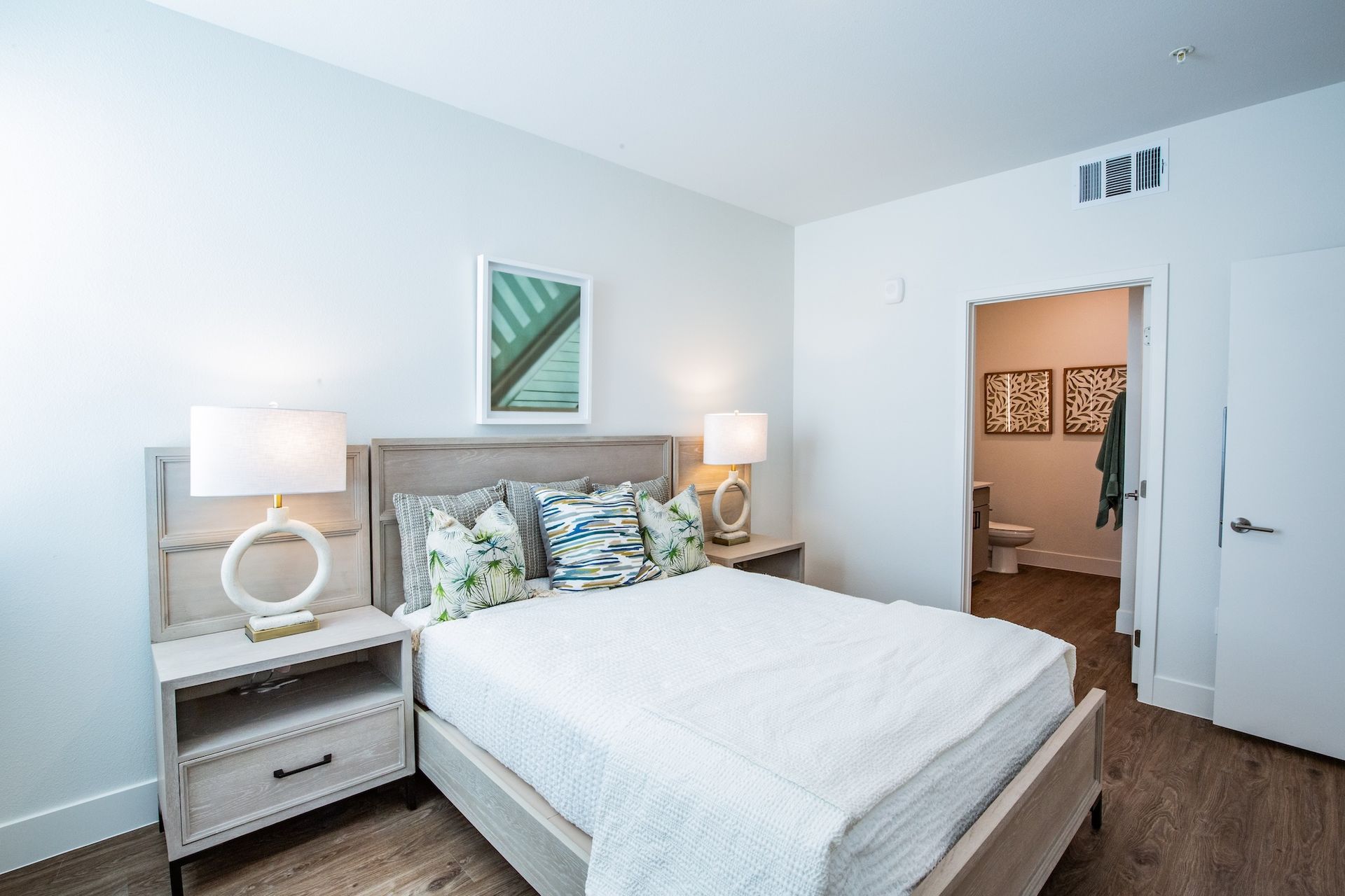 Bedroom with a bed, nightstands, lamps, artwork, and a bathroom visible.