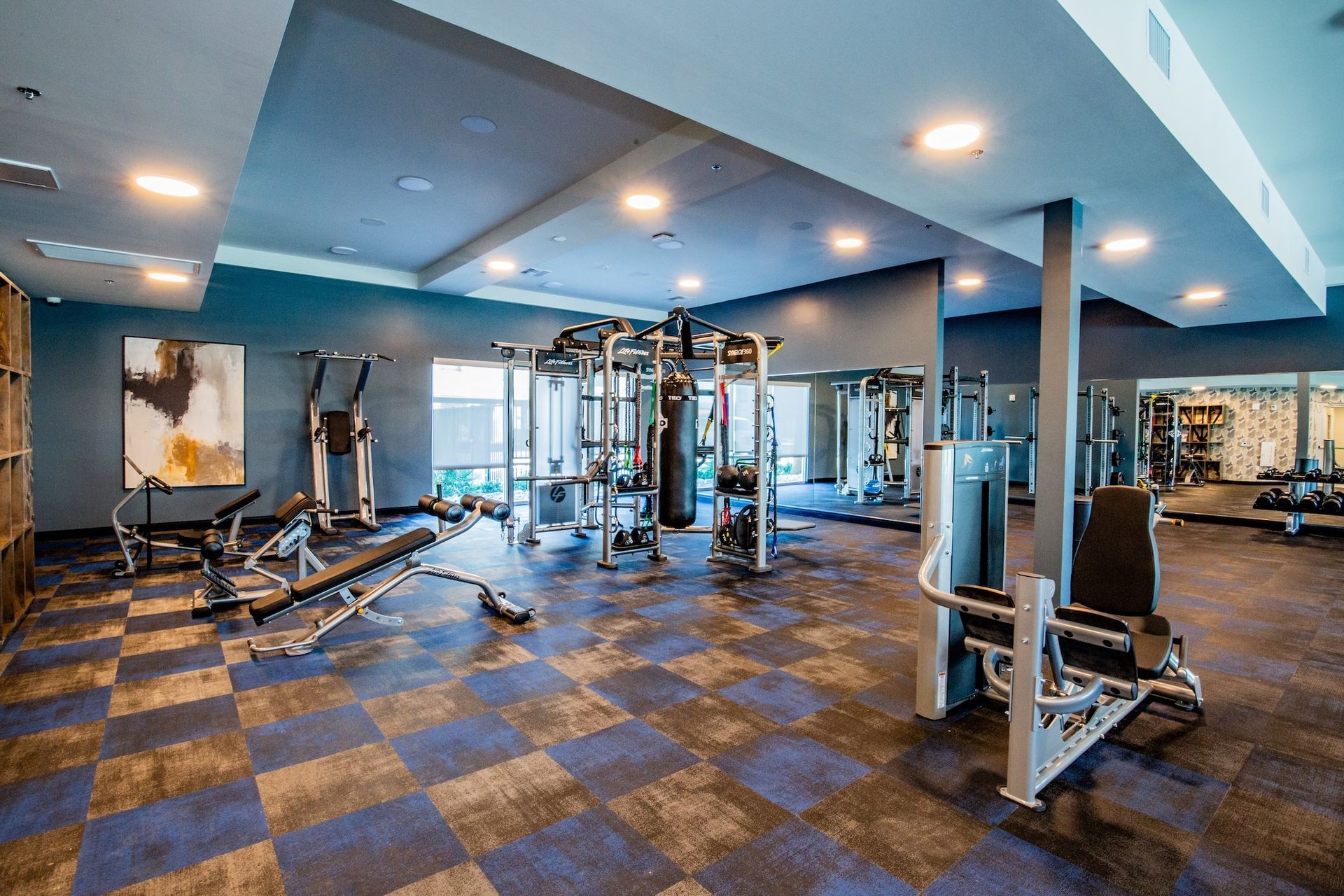 Gym with blue and black checkered floor, workout equipment, and mirrors.
