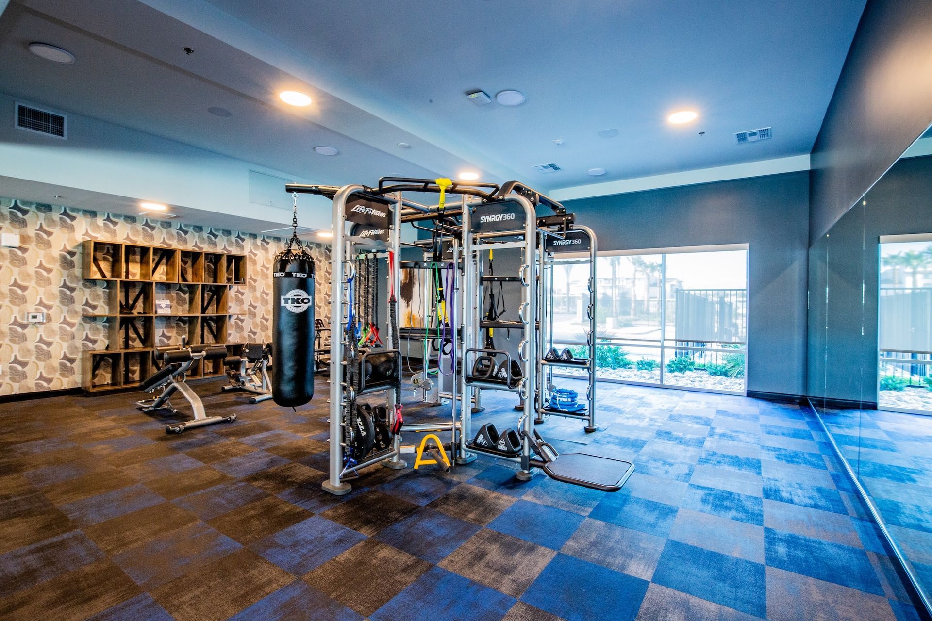 Gym interior with blue and black patterned flooring, weight machines, and a punching bag.