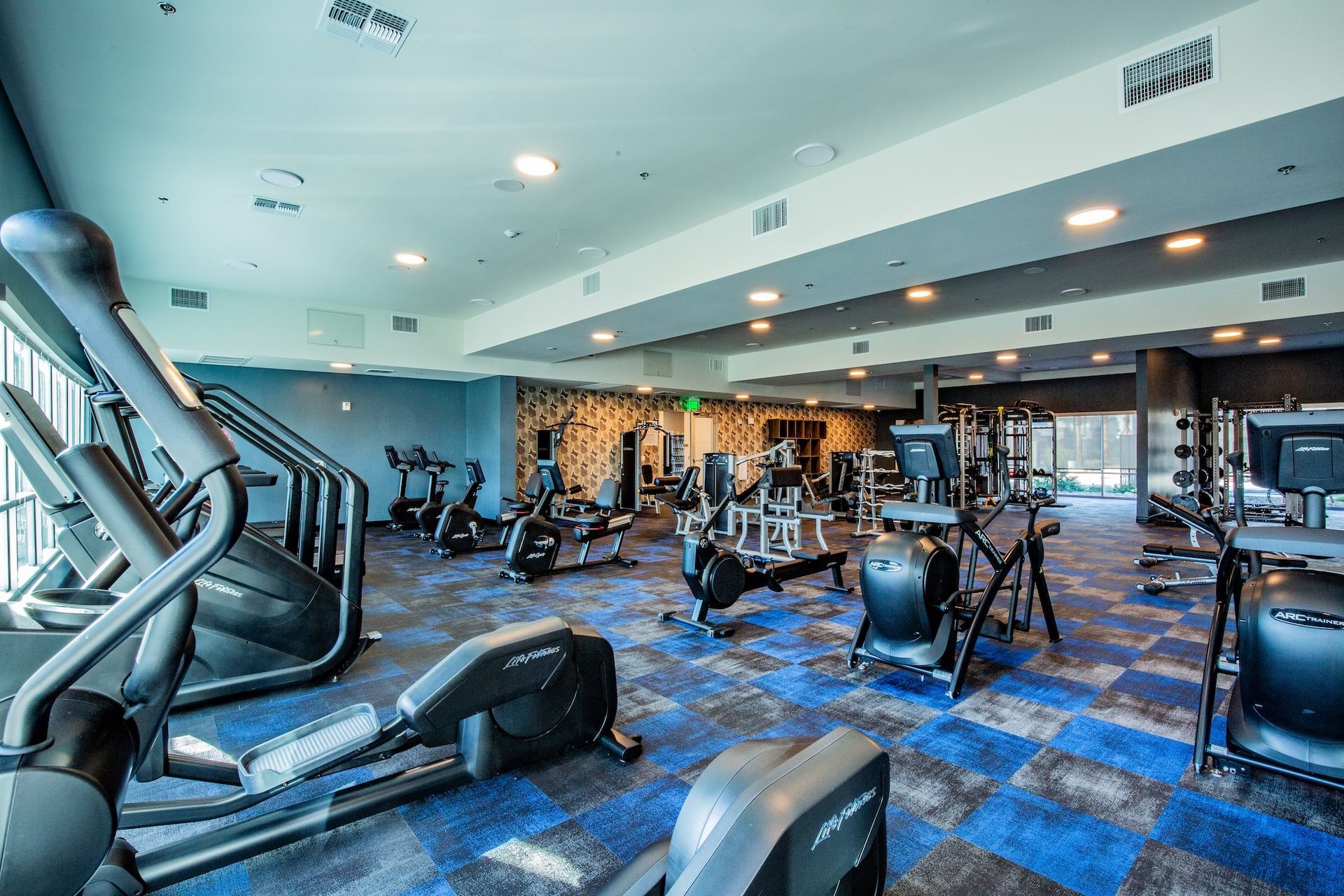 Gym interior with exercise equipment on blue and gray patterned carpet.
