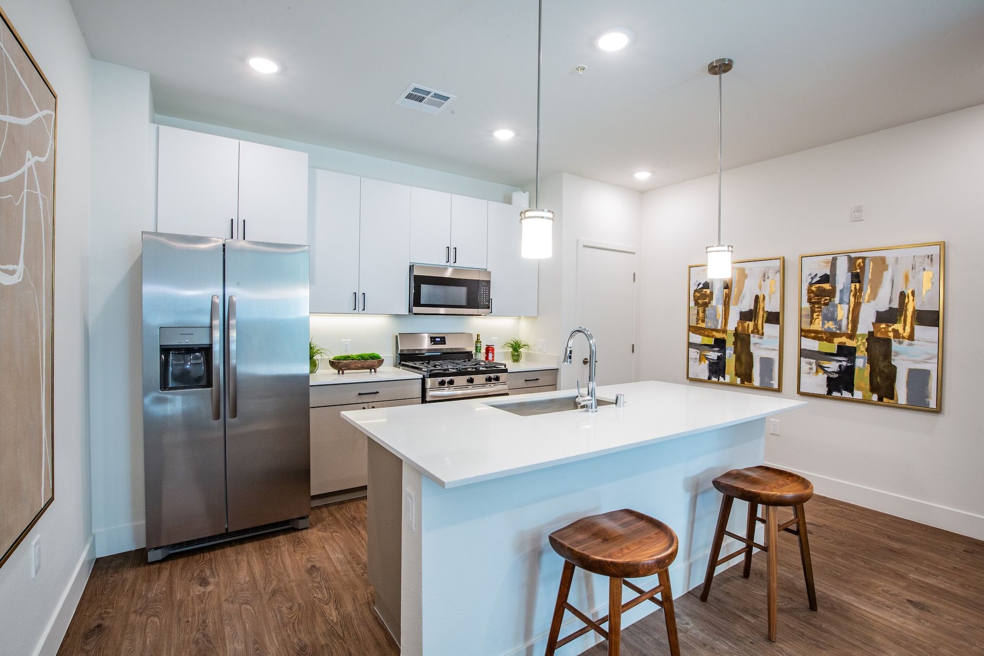 Modern kitchen with white cabinets, island, stainless steel appliances, and wooden stools.
