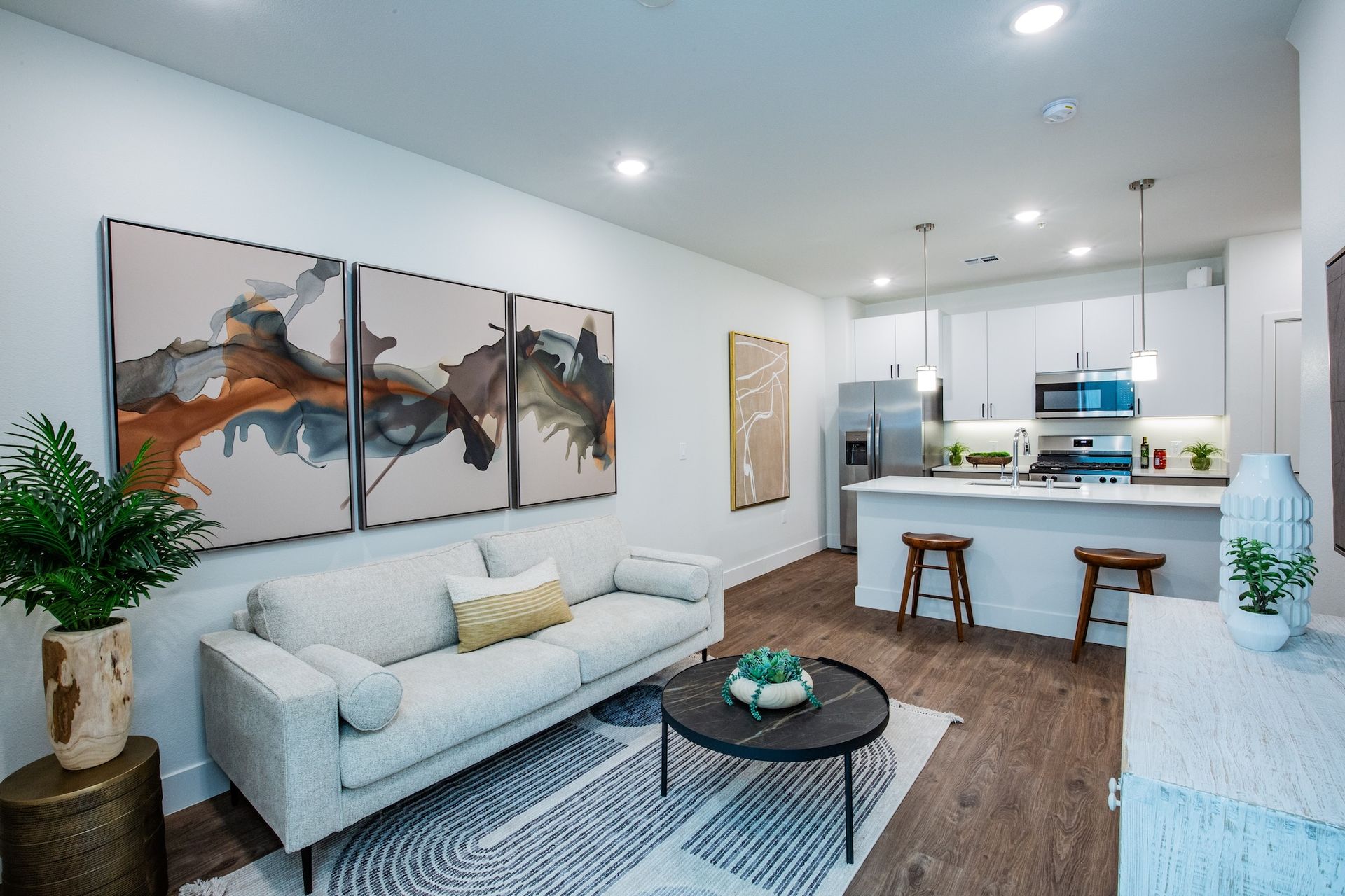 Modern living room with artwork, sofa, kitchen, and bar stools.