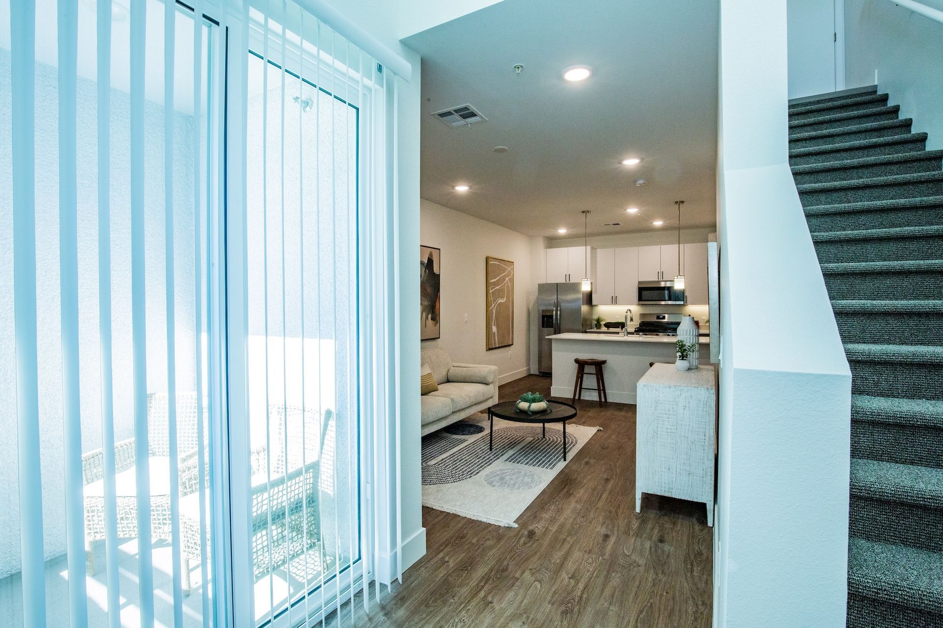 Interior view of a modern apartment with a staircase, kitchen, living area, and sliding glass door to a balcony.