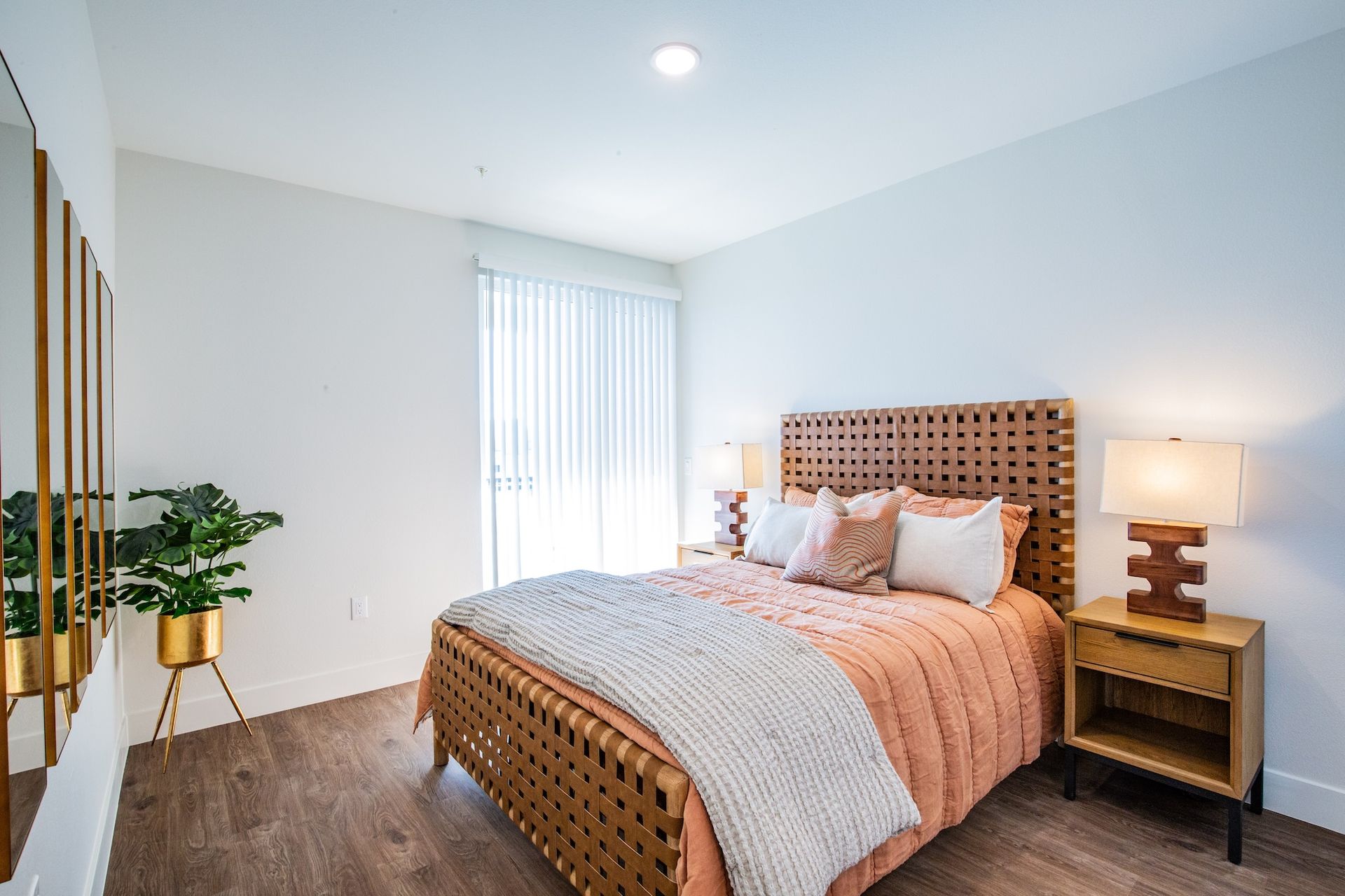 Bedroom with bed, nightstand, mirror, and plant; light peach and neutral tones.