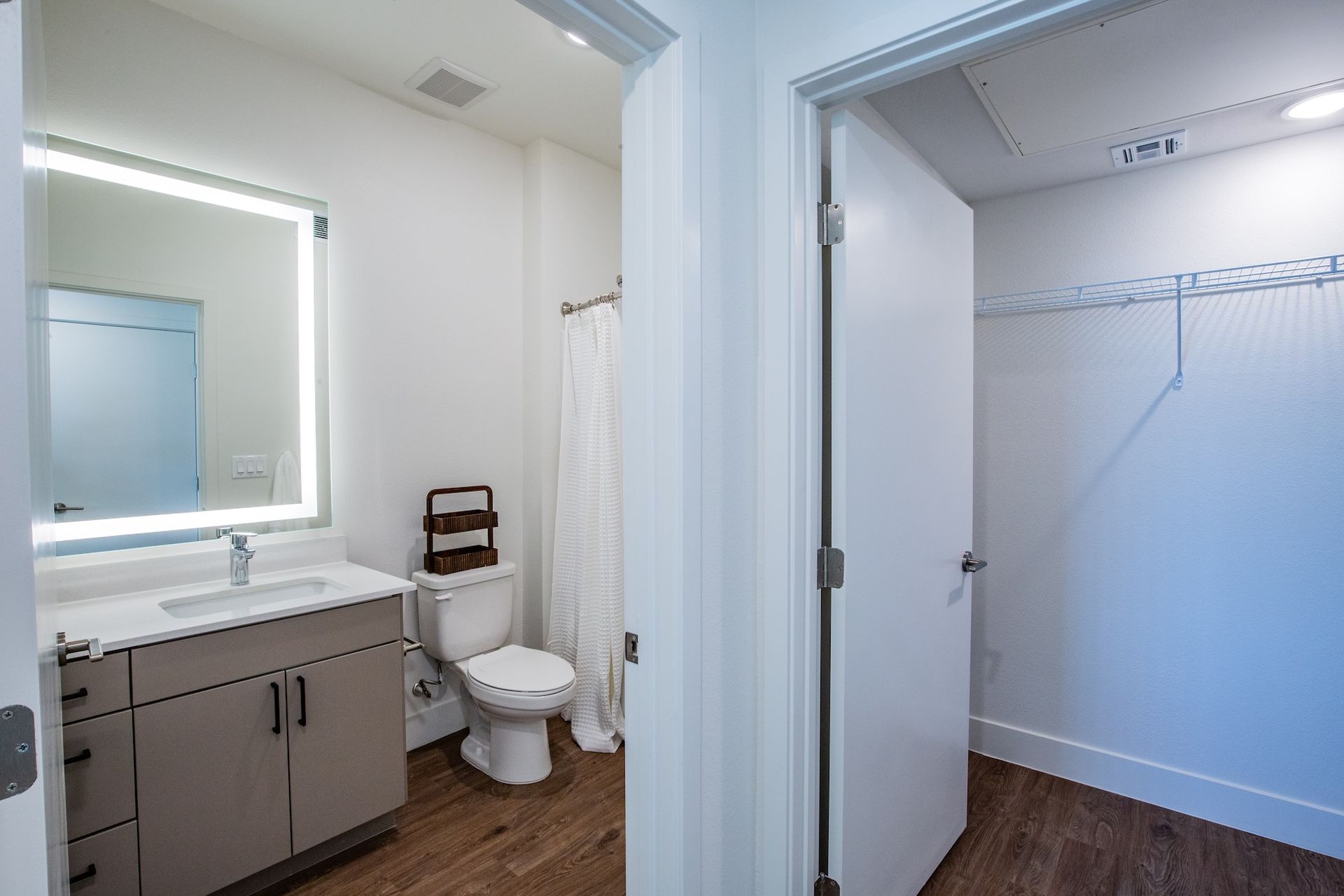 Bathroom with a sink, toilet, shower, and walk-in closet with white walls and wood-look flooring.