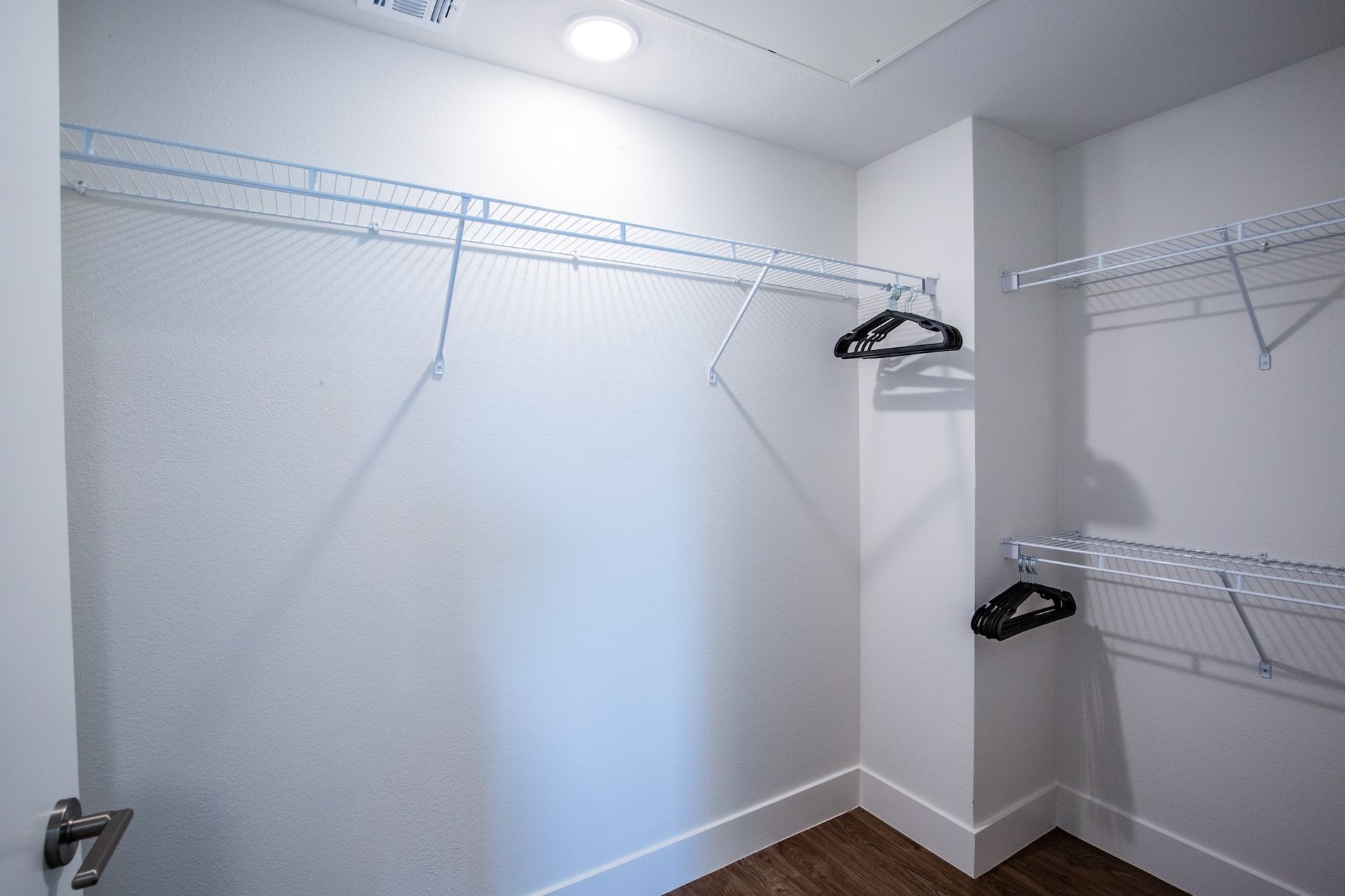 Empty white closet with wire shelving and two black hangers.