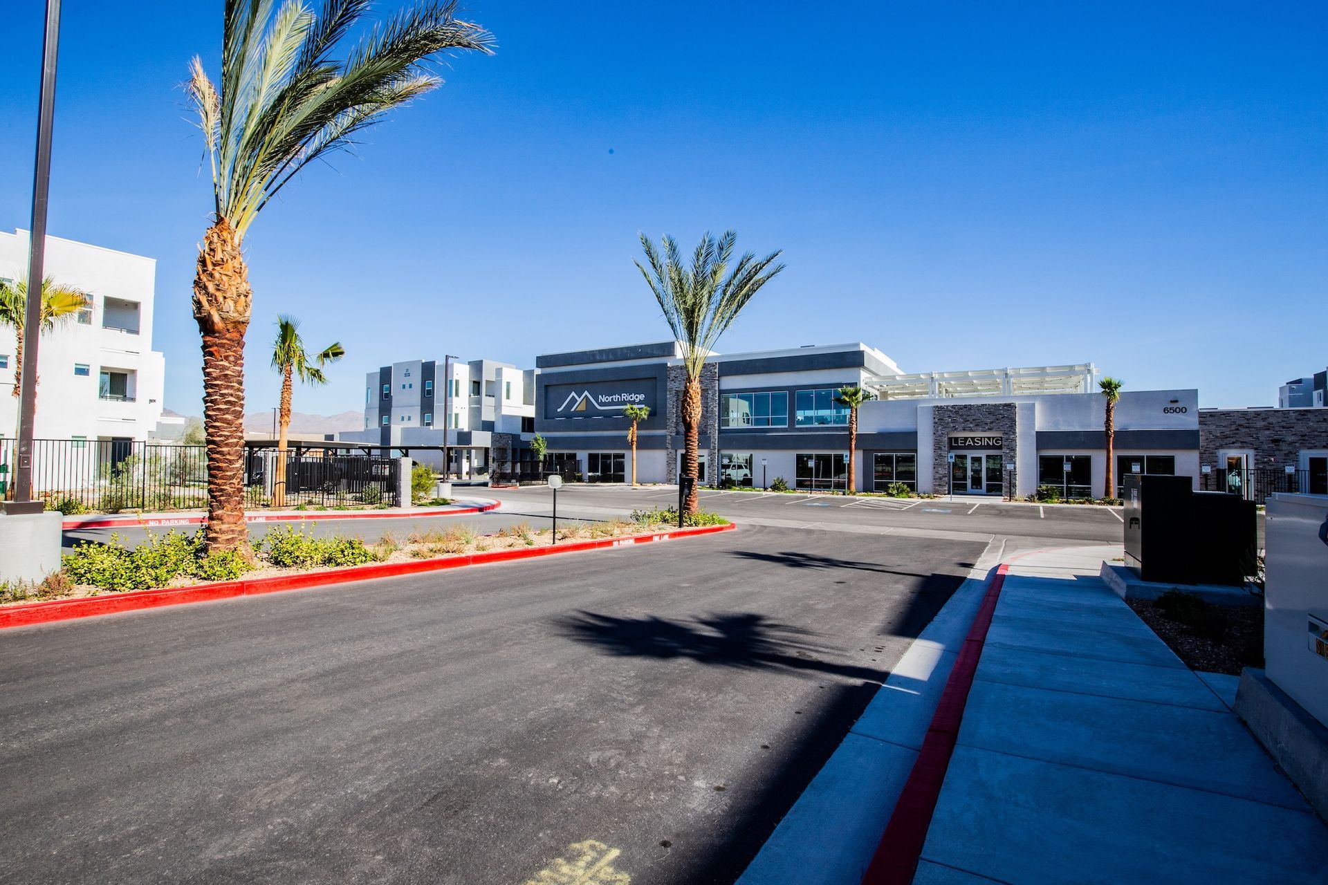Exterior view of modern commercial buildings with palm trees and blue sky.