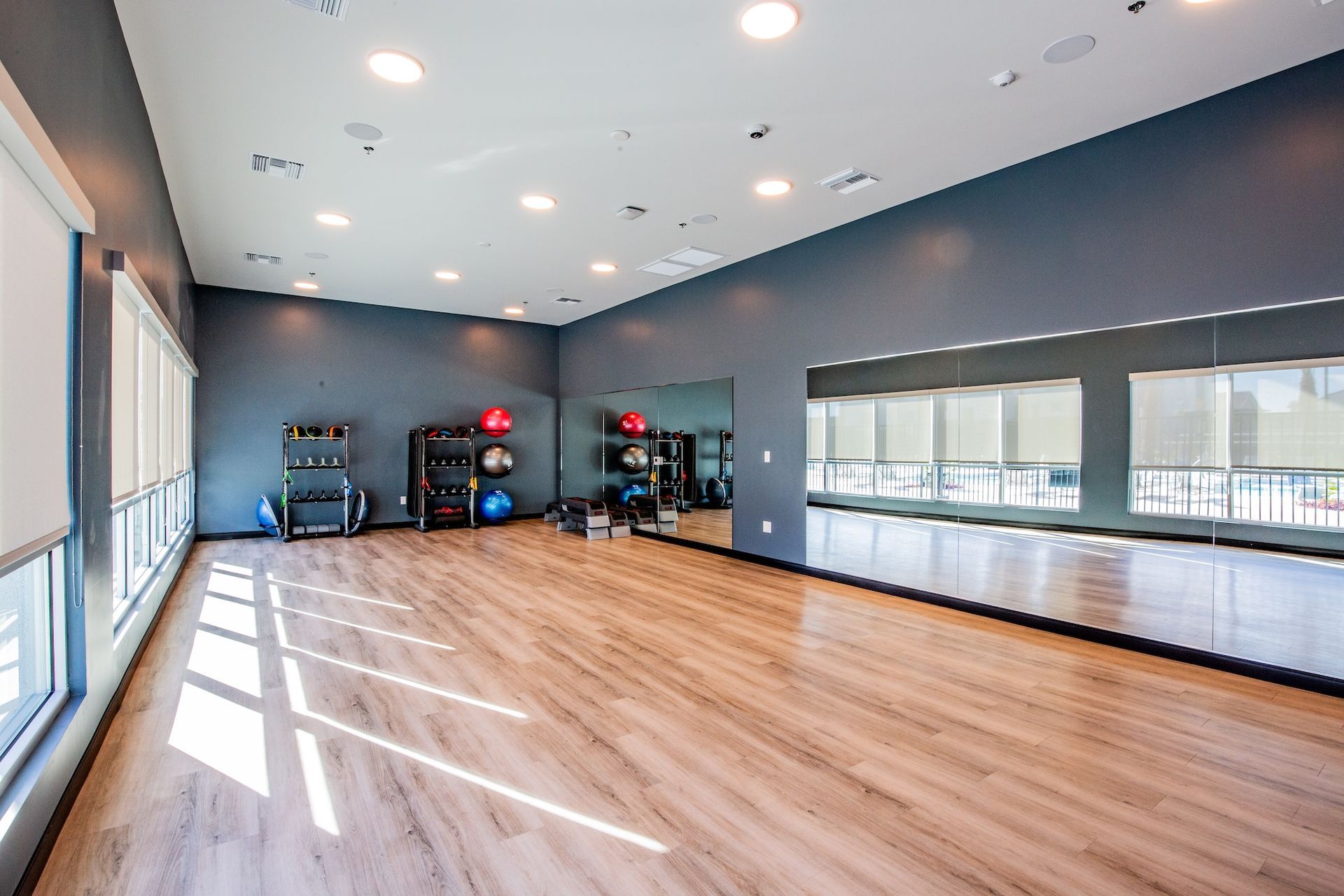 Empty fitness studio with wooden floor, dark blue walls, mirrors, and exercise equipment.