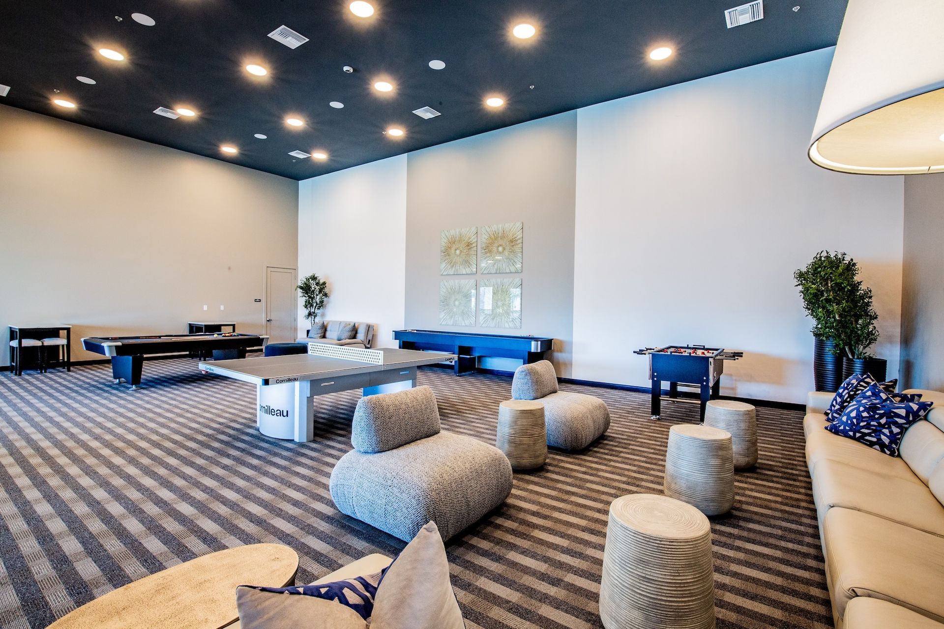 Spacious lounge area with pool table, foosball, sofas, and patterned carpet. Dark ceiling with recessed lights.