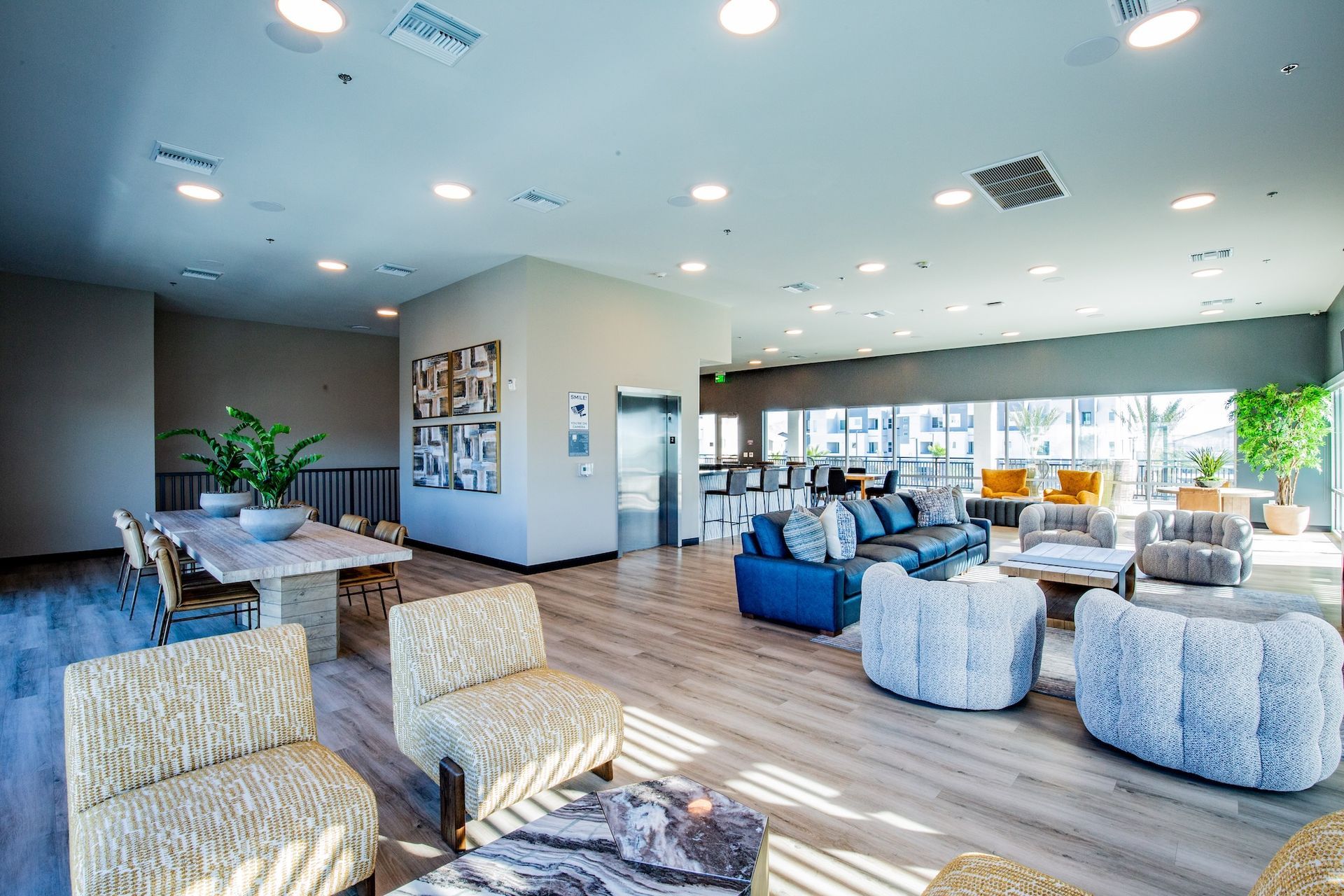 Spacious, modern lounge with light wood floors, various seating, a large table, and a view of a city.