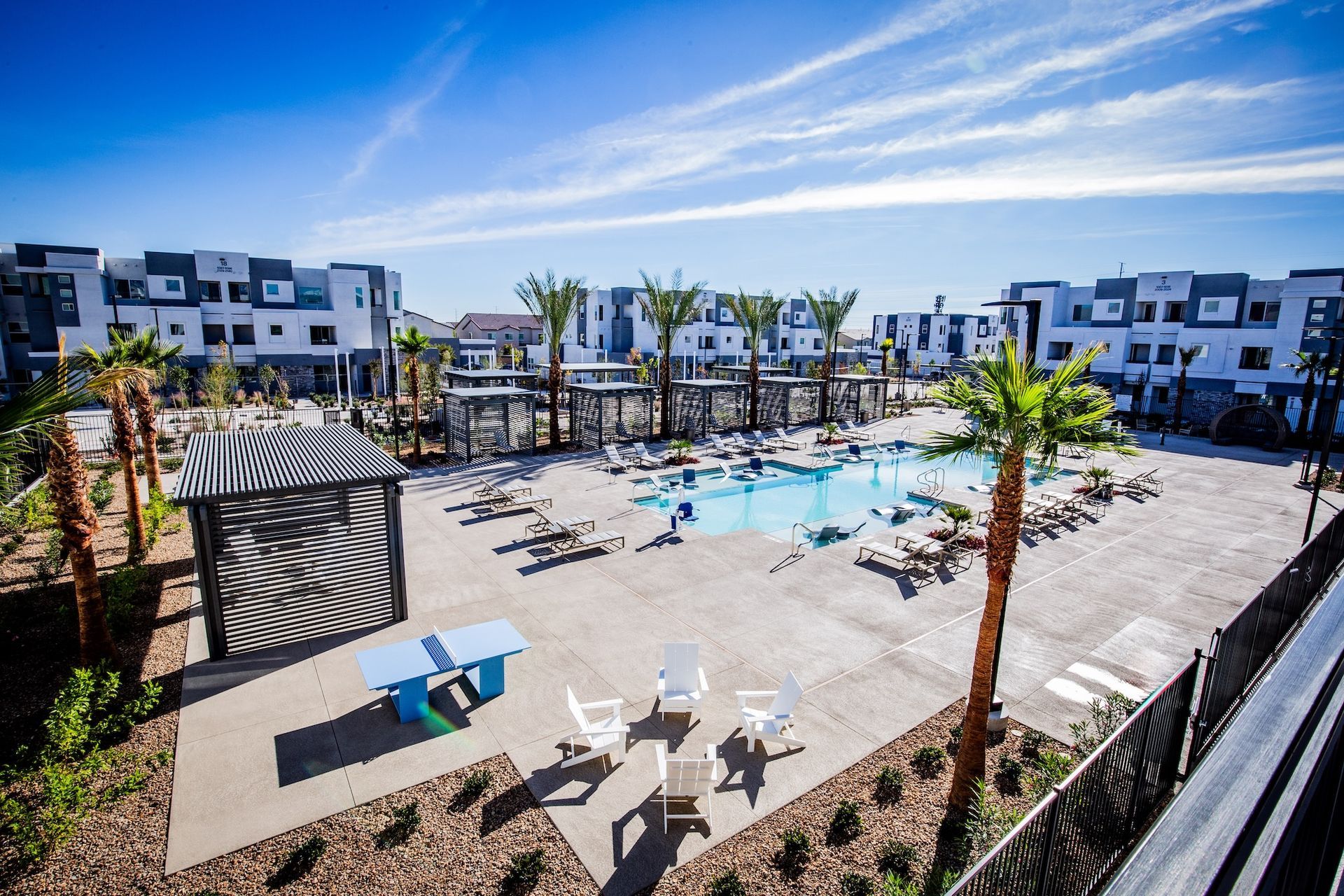 Courtyard with pool, lounge chairs, and modern buildings under a sunny blue sky.