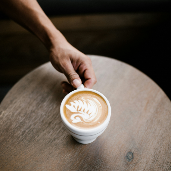 A person is holding a cup of coffee on a wooden table