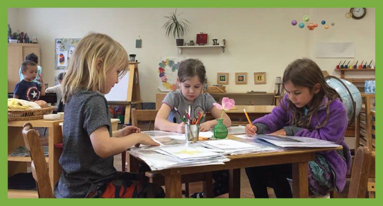 Three children drawing at a table in a classroom.