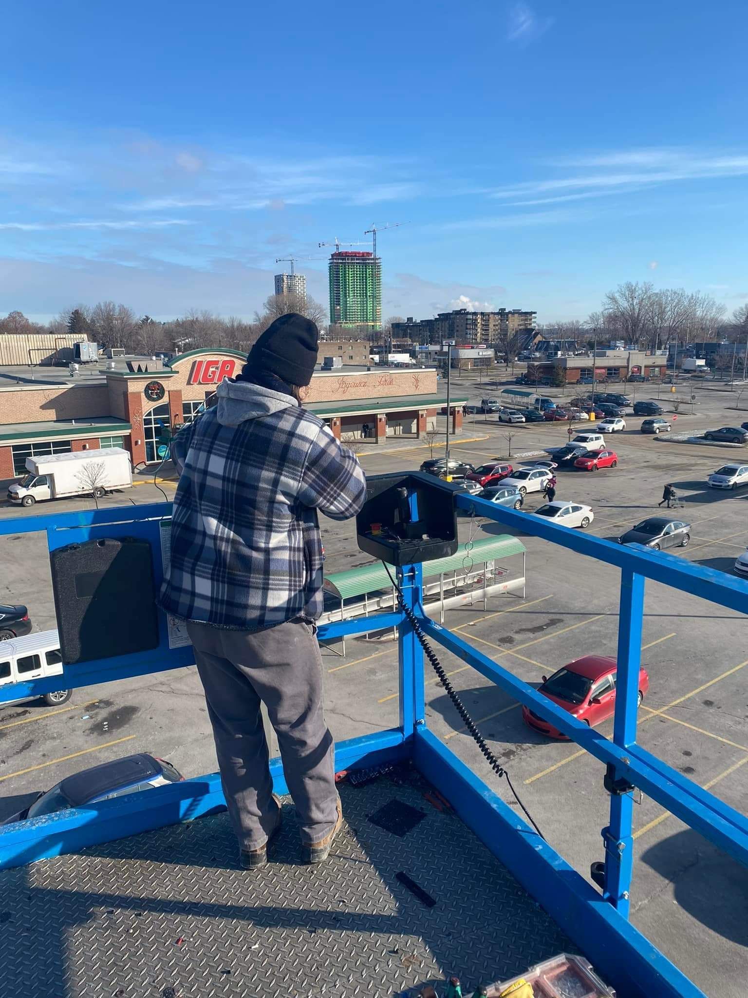 Un homme se tient au sommet d'une grue surplombant un parking.
