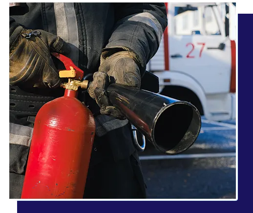 A fireman is holding a red fire extinguisher in front of a fire truck with the number 27 on it.