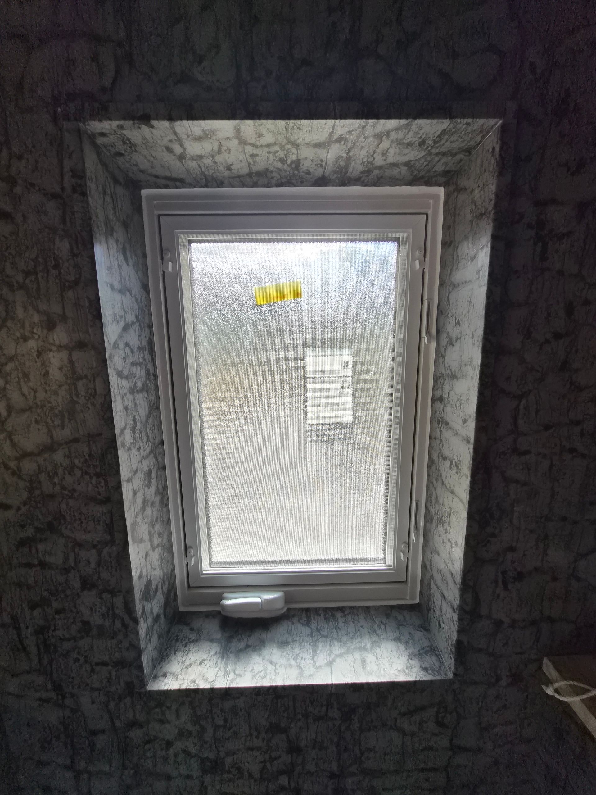 A white window with textured privacy glass set into a deep wall opening finished with dark, patterned wallpaper.