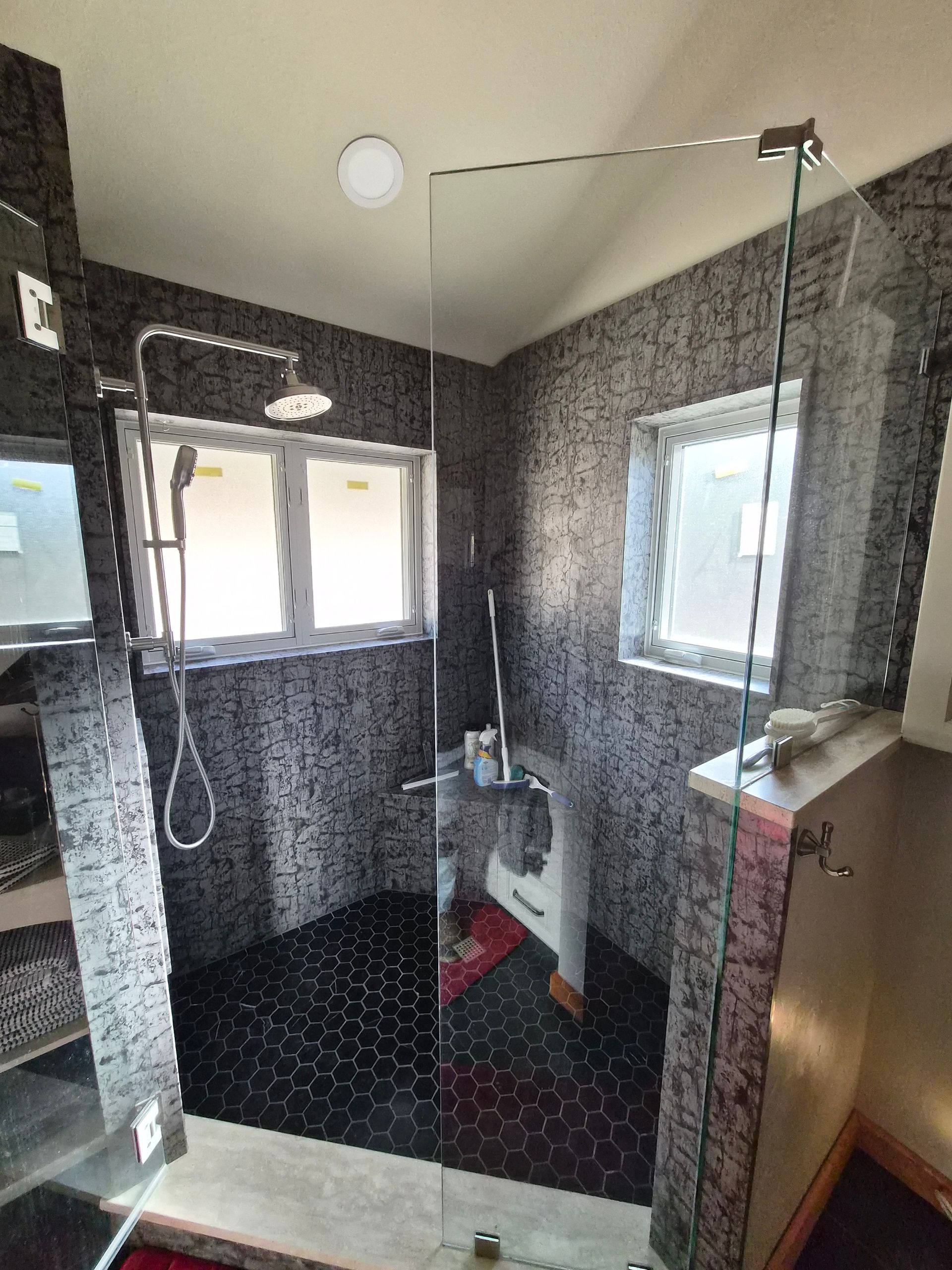 A modern walk-in shower with dark patterned tile walls, a black pebble floor, and a clear glass enclosure.