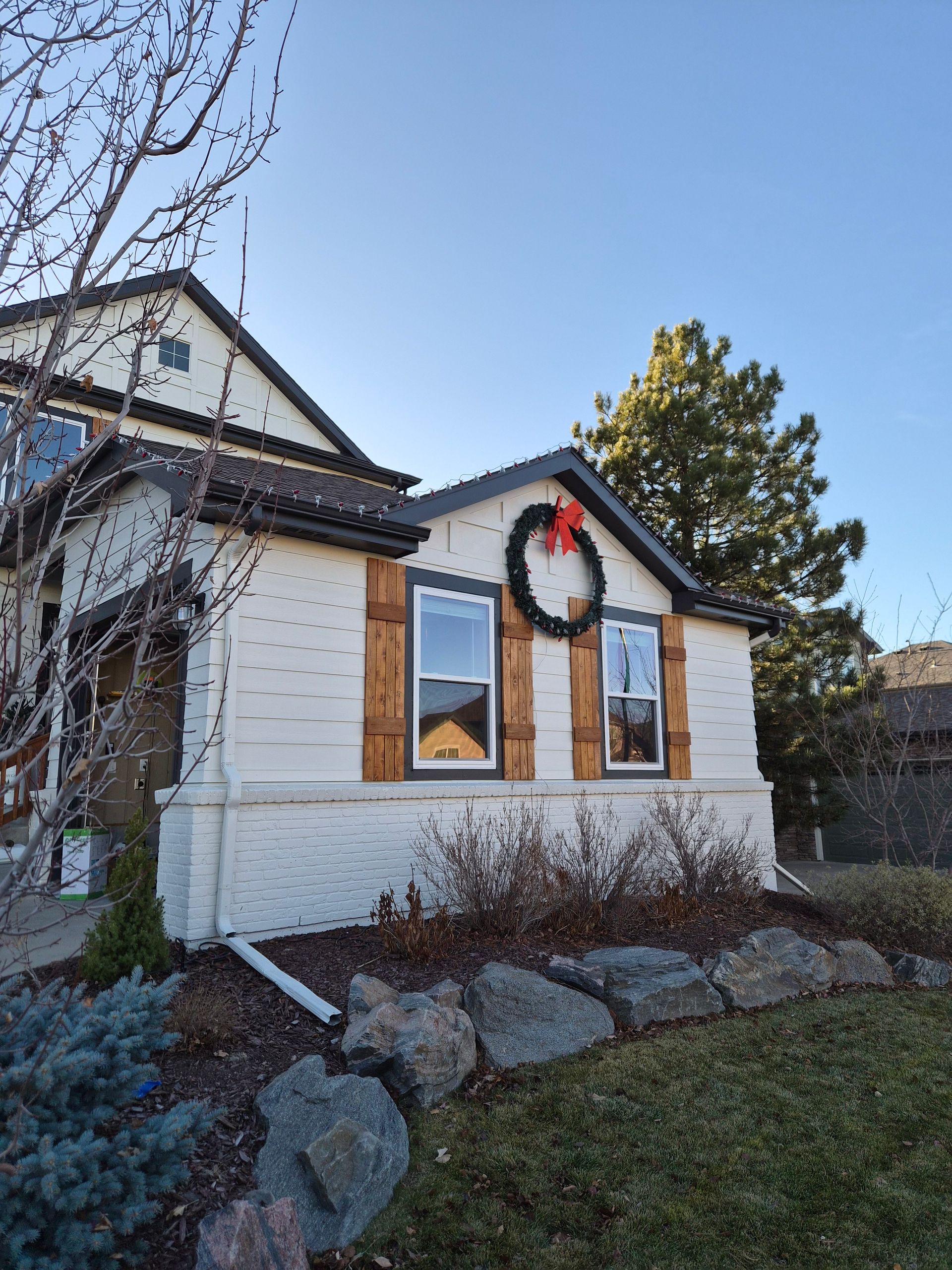 A white house with wood shutters and a decorative wreath on the front wall, set against a clear blue sky.