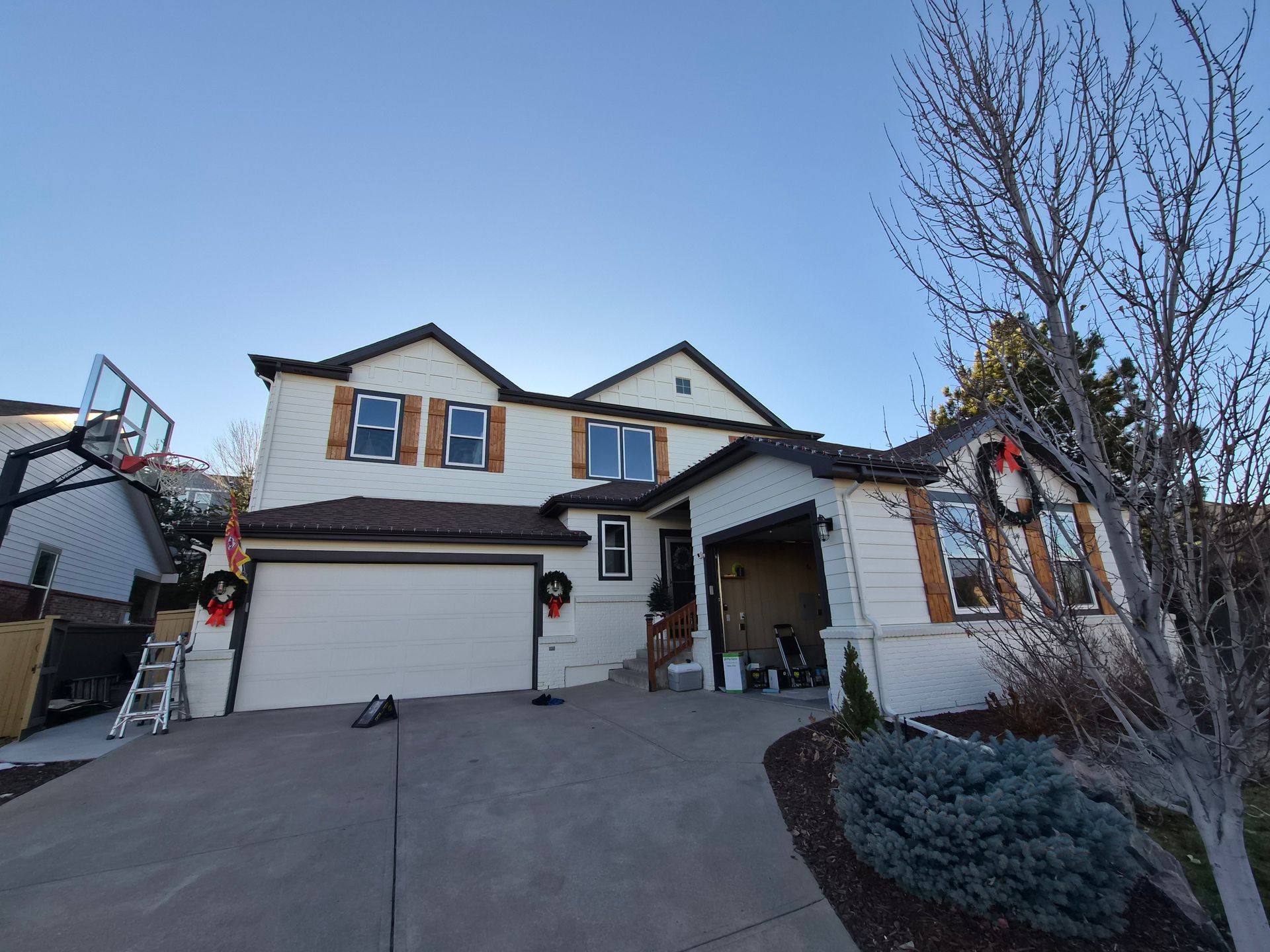 Two-story suburban house with white siding, wood accents, a double garage, and holiday wreaths during the daytime.