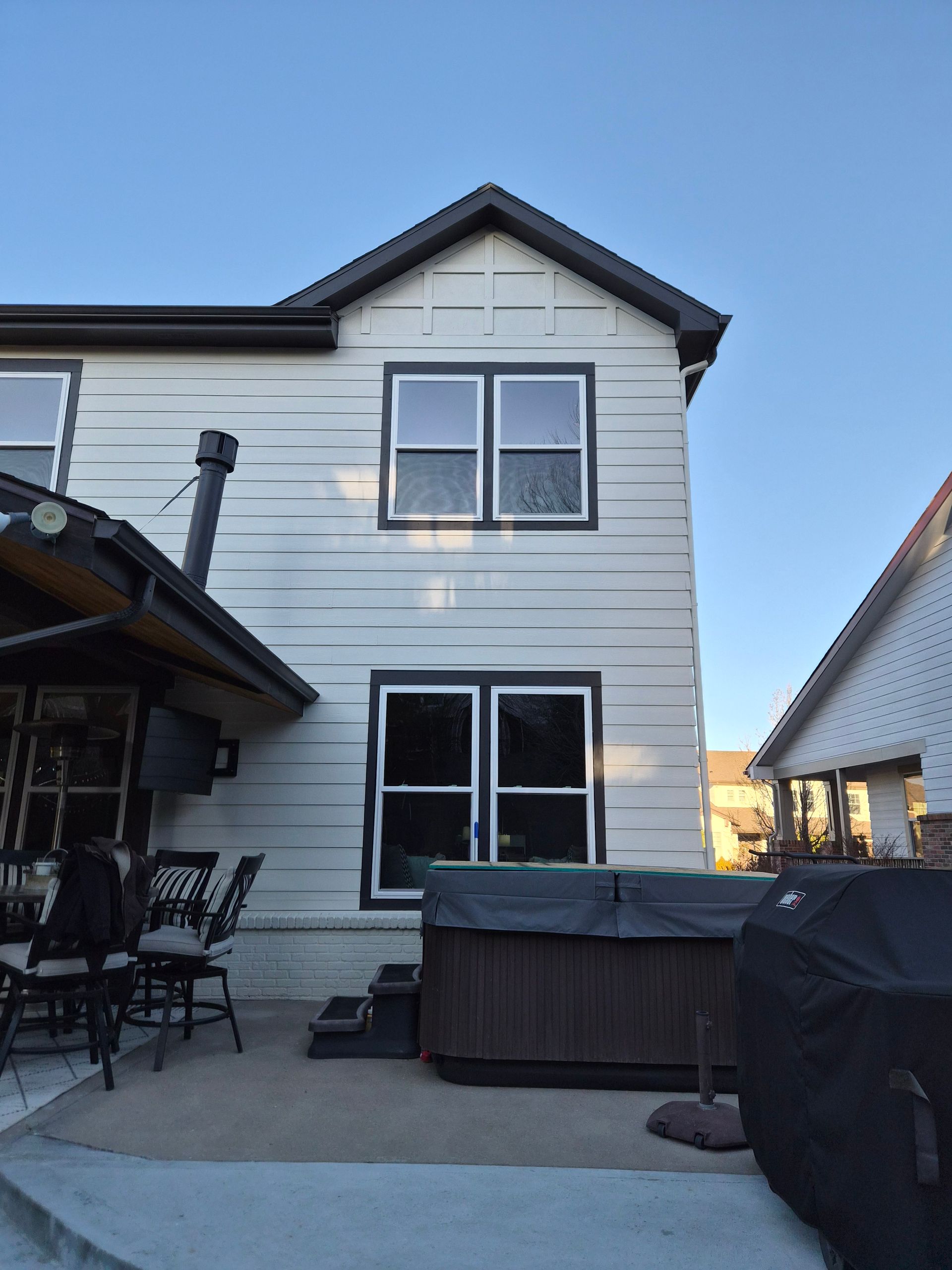 A side view of a white, two-story house exterior with a hot tub on a patio, adjacent to a covered outdoor seating area.
