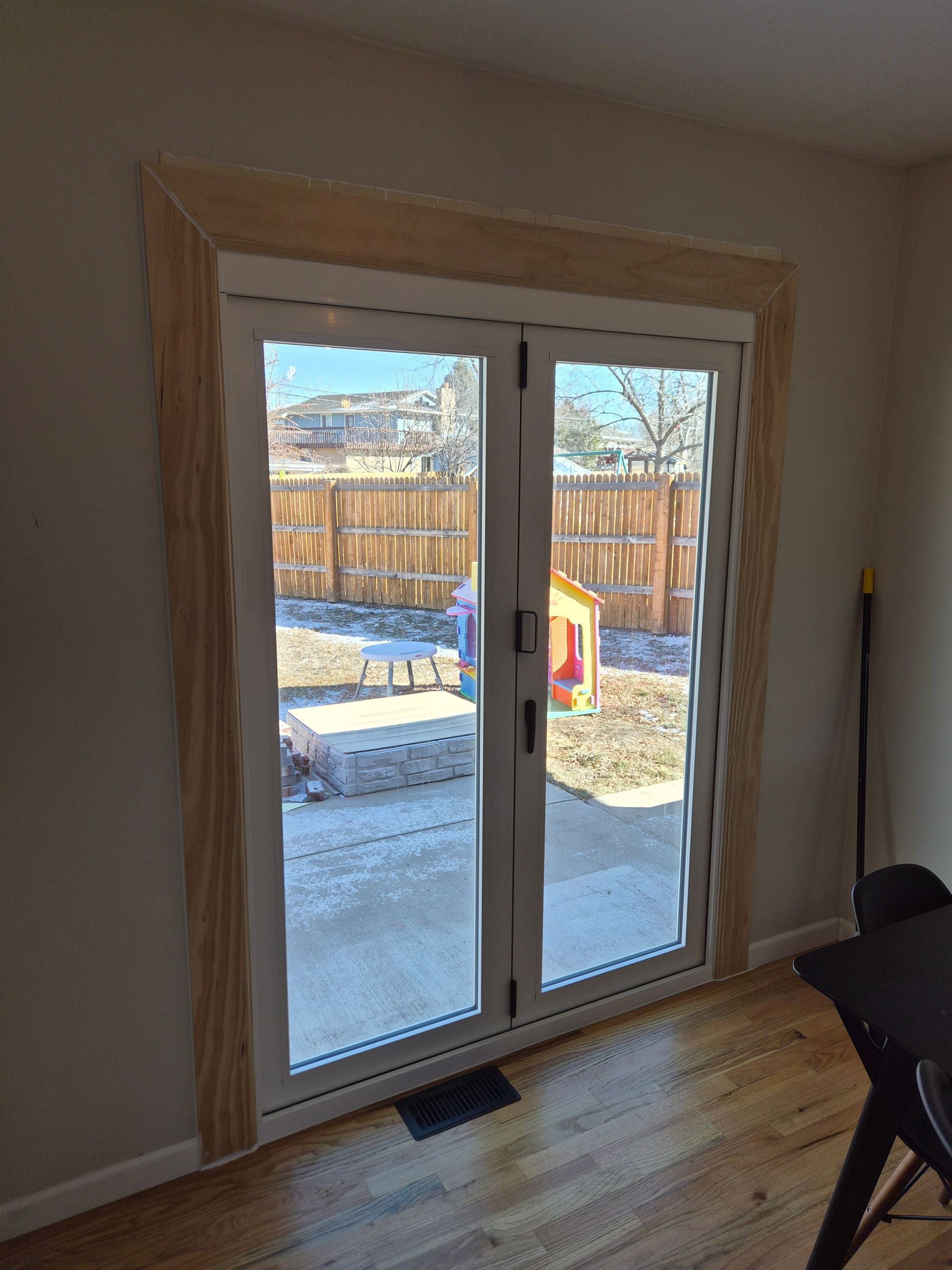 A set of glass French doors leading to a backyard, framed by unfinished light-colored wooden trim in a home interior.