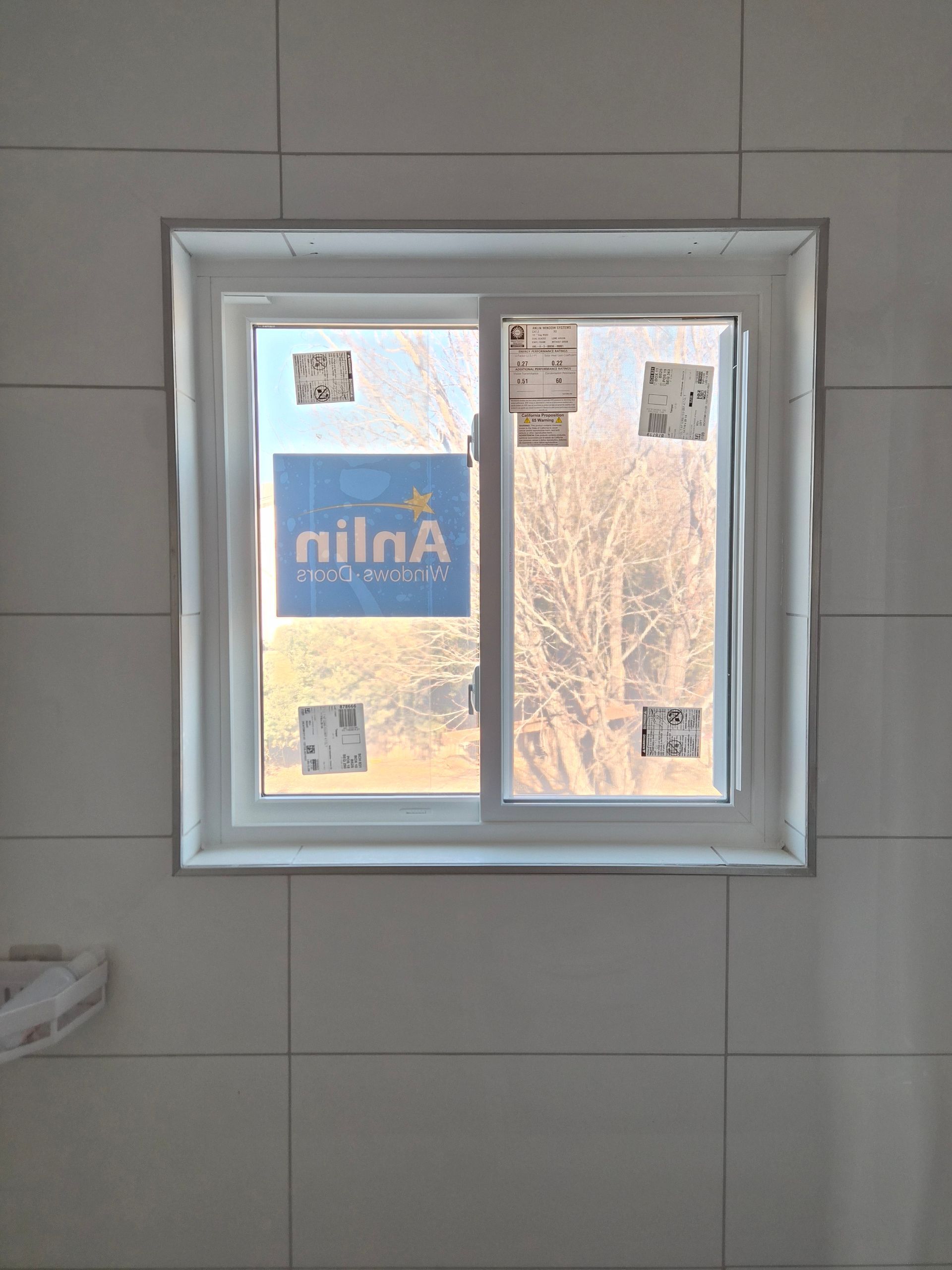 A white sliding window installed in a tiled wall with a brand logo sticker on the glass.