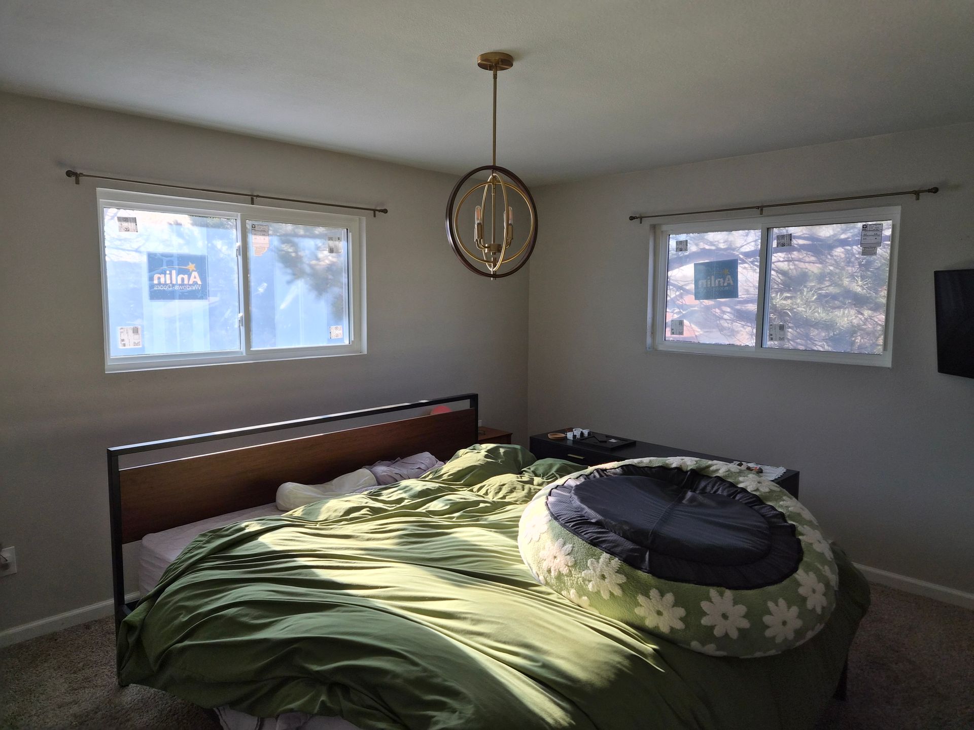 A bedroom with a bed covered in a green blanket, a circular dog bed, and a gold orb-style pendant light hanging above.