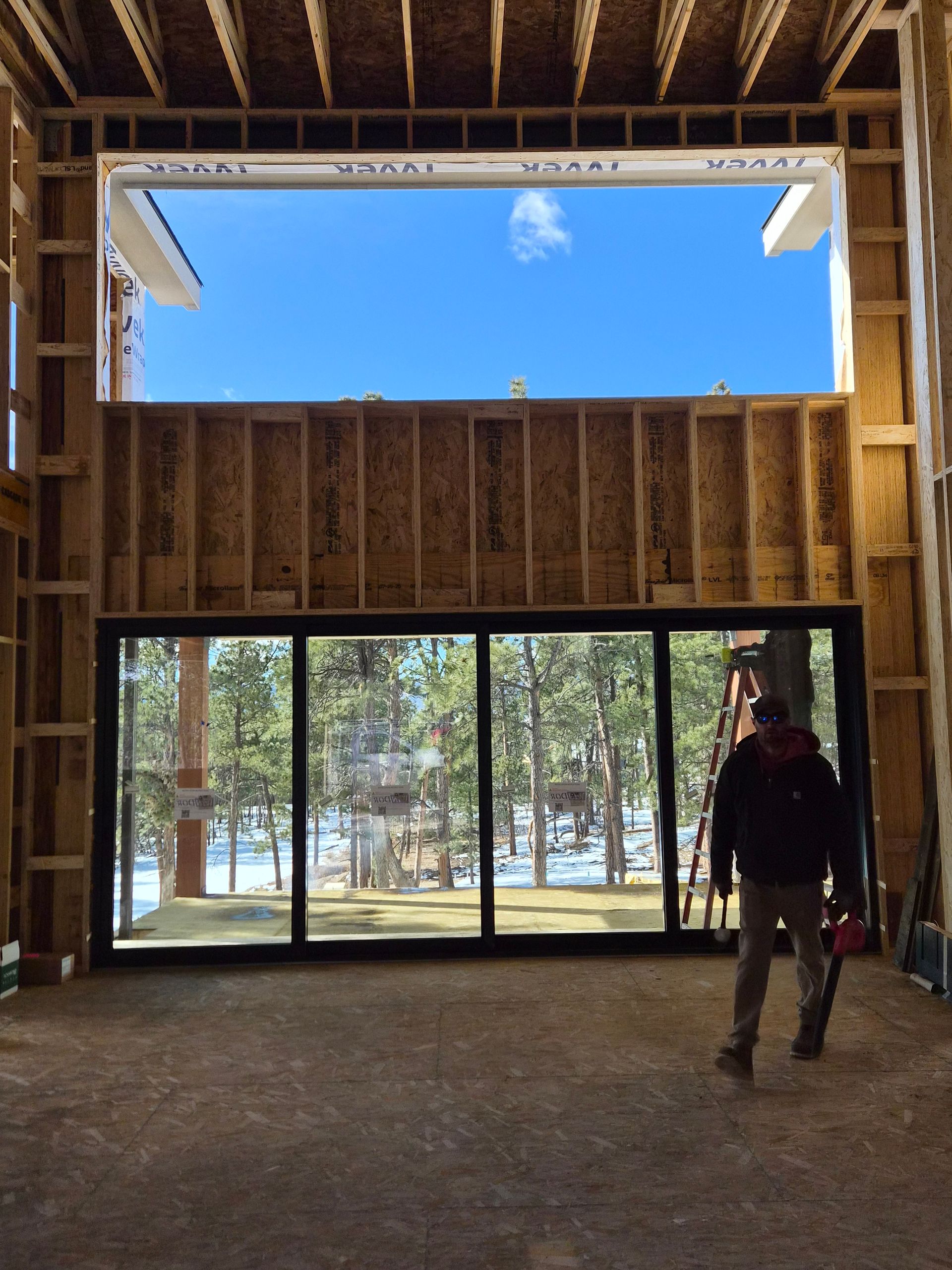 An interior construction scene featuring a large floor-to-ceiling glass wall, an upper window, and a worker standing.