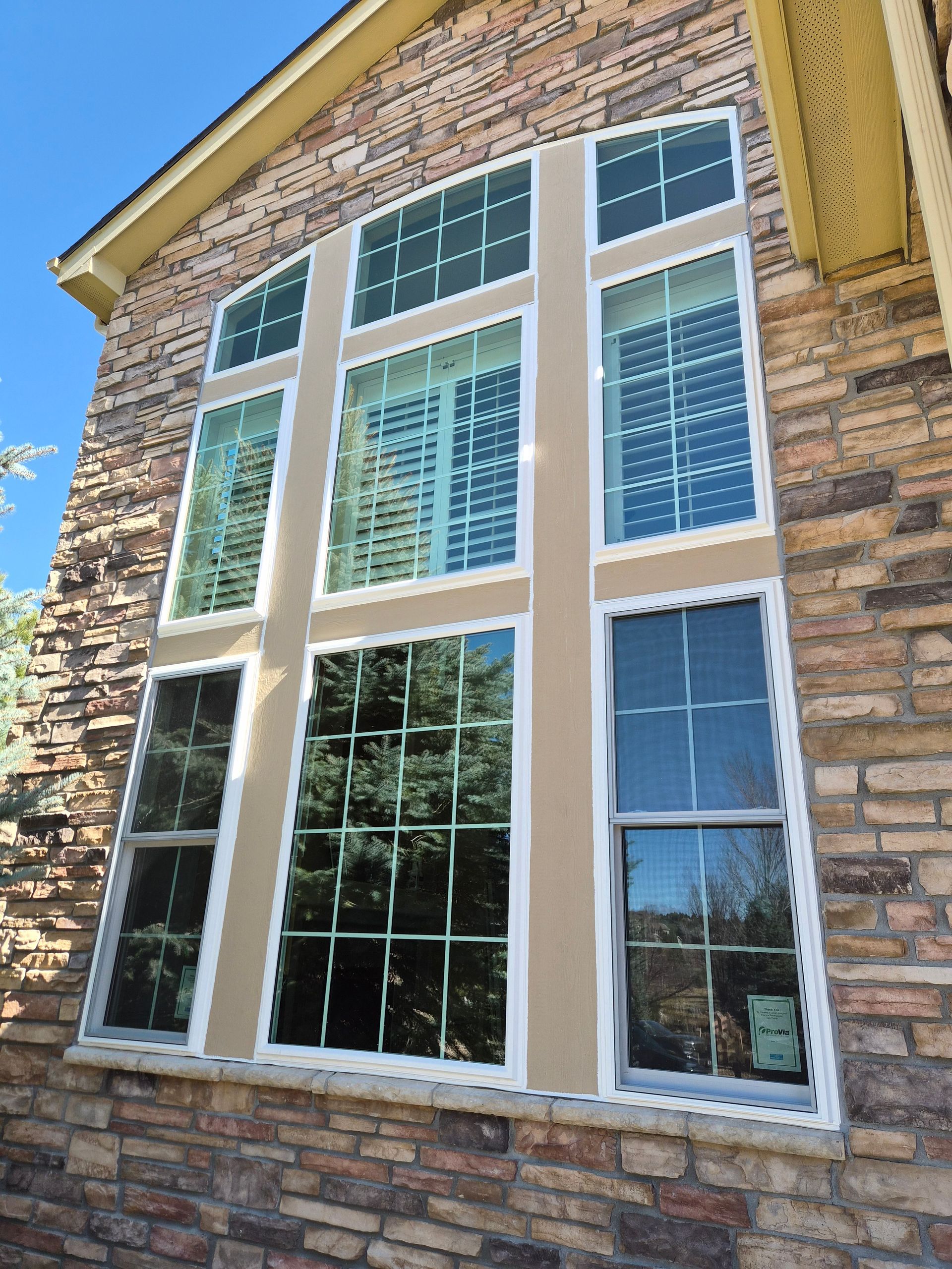 A large, multi-paneled window with white frames set into a textured, multi-colored stone exterior wall.