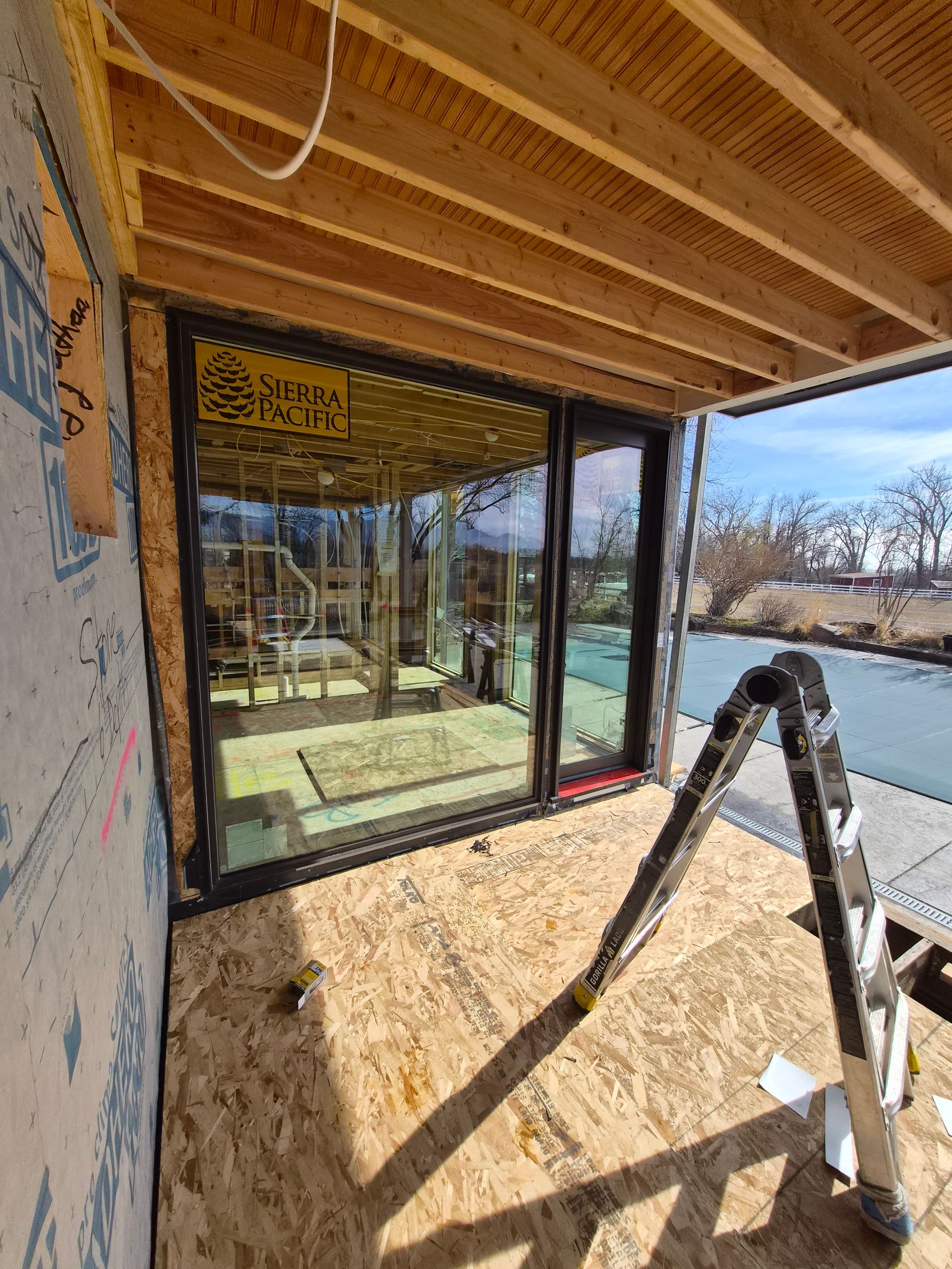 A construction site featuring an installed sliding glass door, exposed wooden ceiling joists, and a metal ladder.