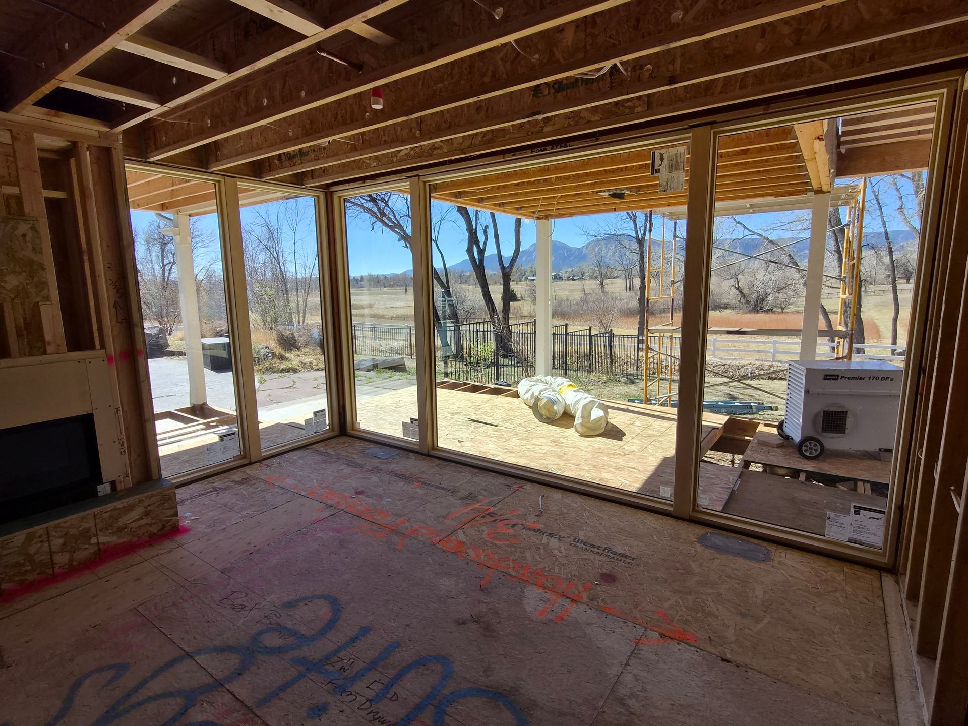 Interior of a house under construction with a large open wall frame looking out onto a backyard with distant mountains.