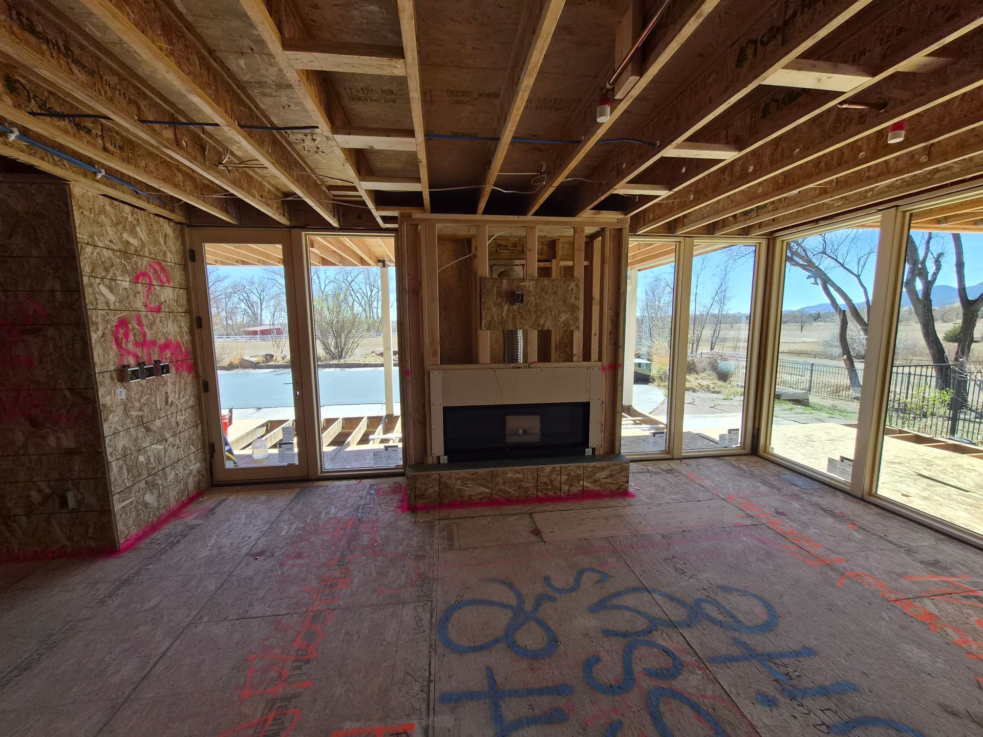 Interior view of a residential construction site featuring an unfinished wooden fireplace frame and large glass windows.