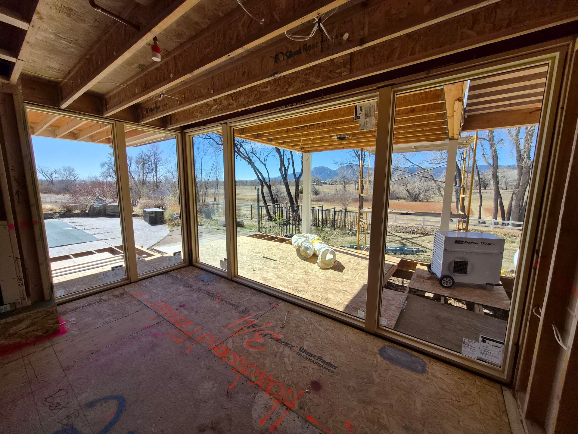 Unfinished interior room with large glass doors opening to a view of a desert landscape and a wooden patio structure.